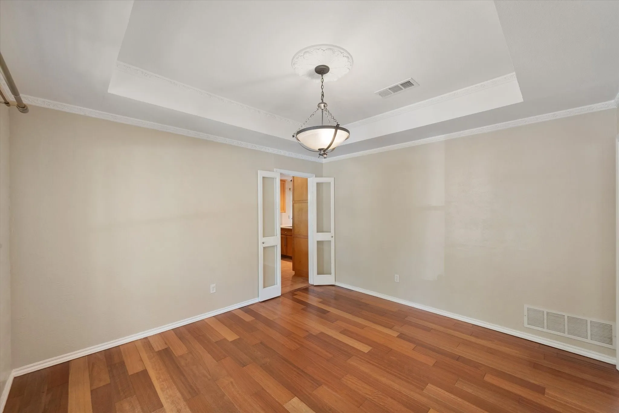 Tray ceiling featuring a decorative ceiling medallion, wood-finish flooring, and double glass-paneled doors