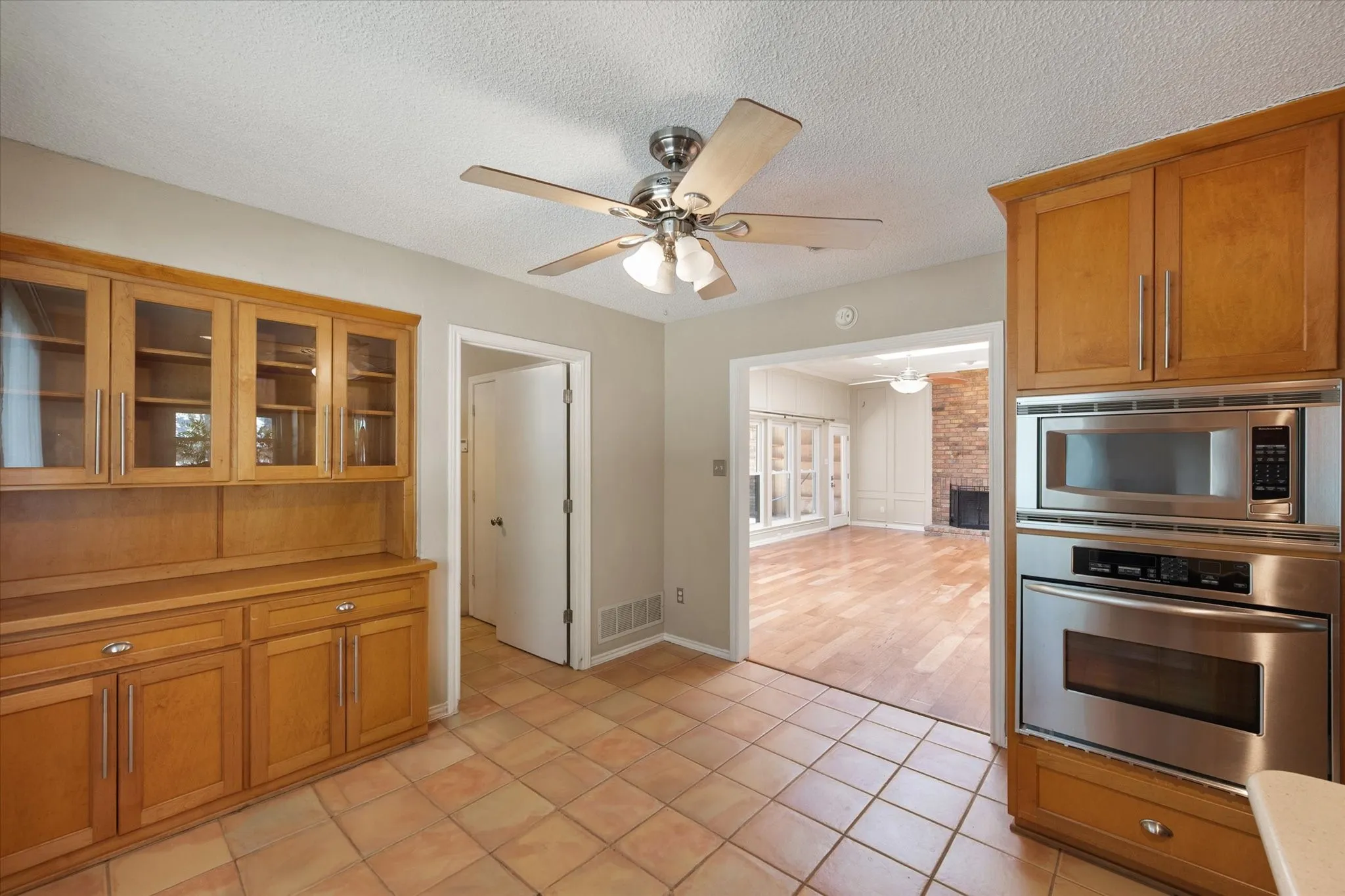 Custom wood cabinetry featuring glass-front display uppers, integrated stainless steel double wall oven and microwave, and ceramic tile flooring