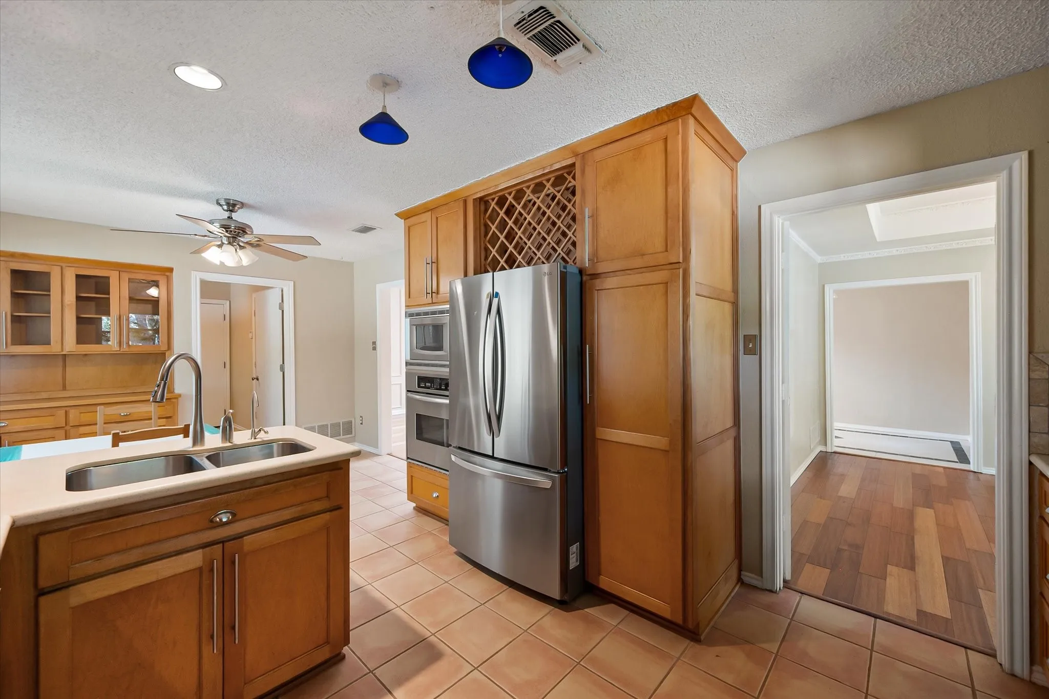 Kitchen featuring light wood cabinetry with built-in wine storage, stainless steel appliances including a double wall oven, dual-basin sink, and ceramic tile flooring