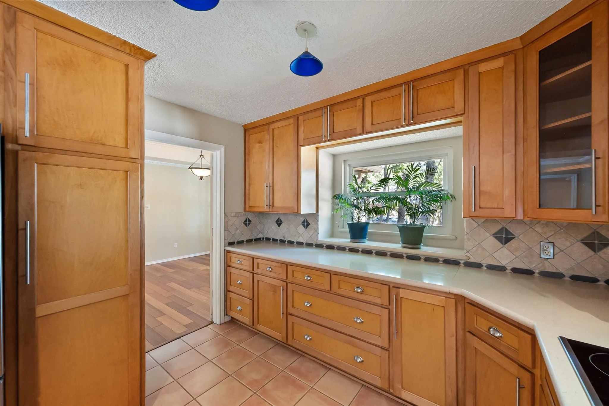 Kitchen featuring natural wood cabinetry, quartz countertops, tile backsplash with decorative accents, built-in glass-front display cabinetry, and a garden window