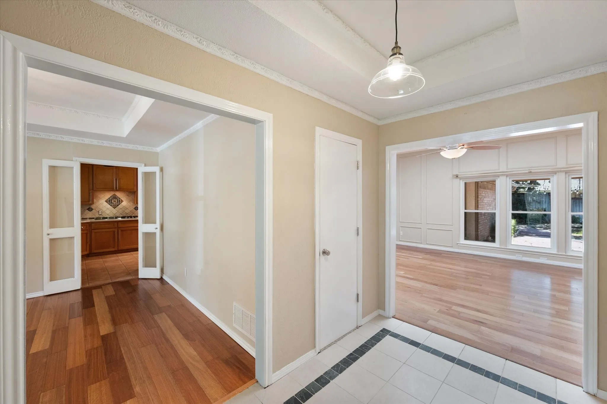 Foyer featuring tile flooring with a decorative border, wood-finish flooring, tray ceilings with crown molding, and glass-paneled French doors