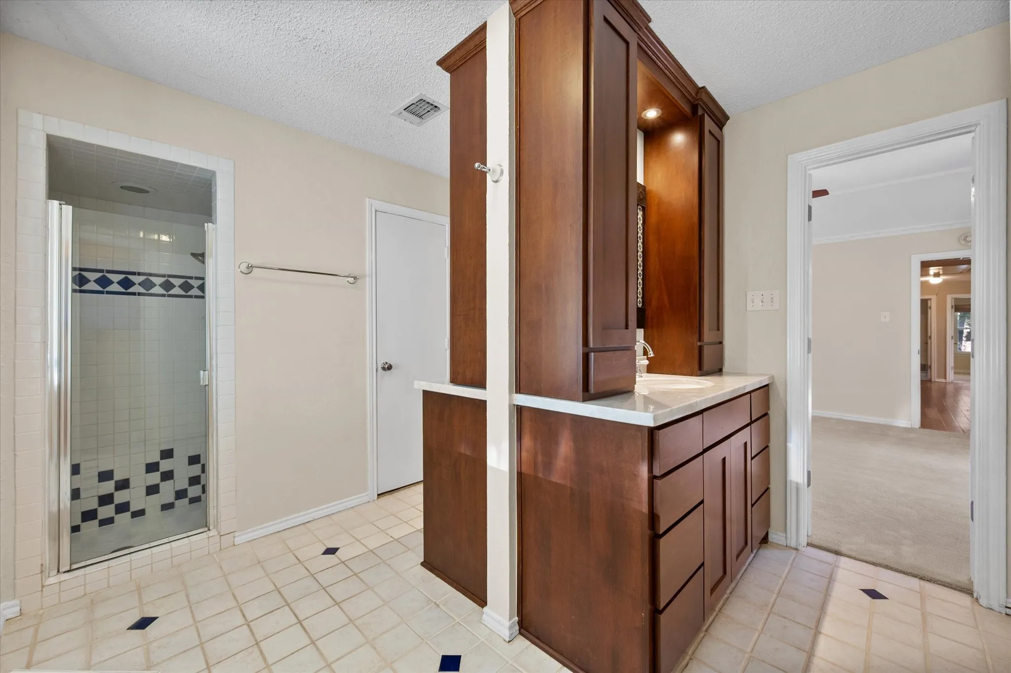 Bathroom featuring a custom wood-finish cabinetry vanity with a stone countertop, a walk-in shower with glass enclosure and decorative tile accents, and tiled flooring with inset tile details