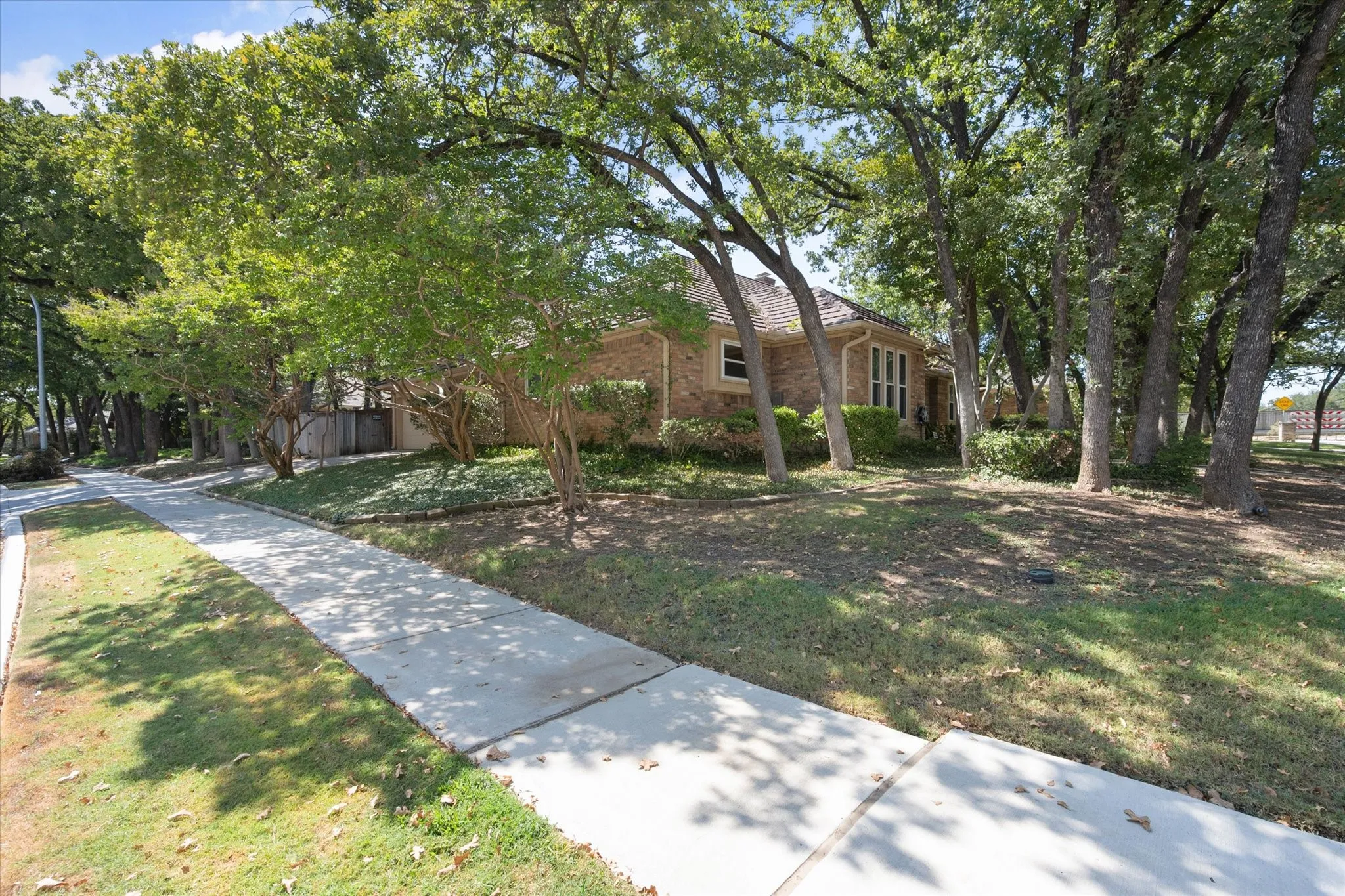 Brick exterior featuring a multi-gabled roofline, concrete sidewalk, and mature hardwood trees