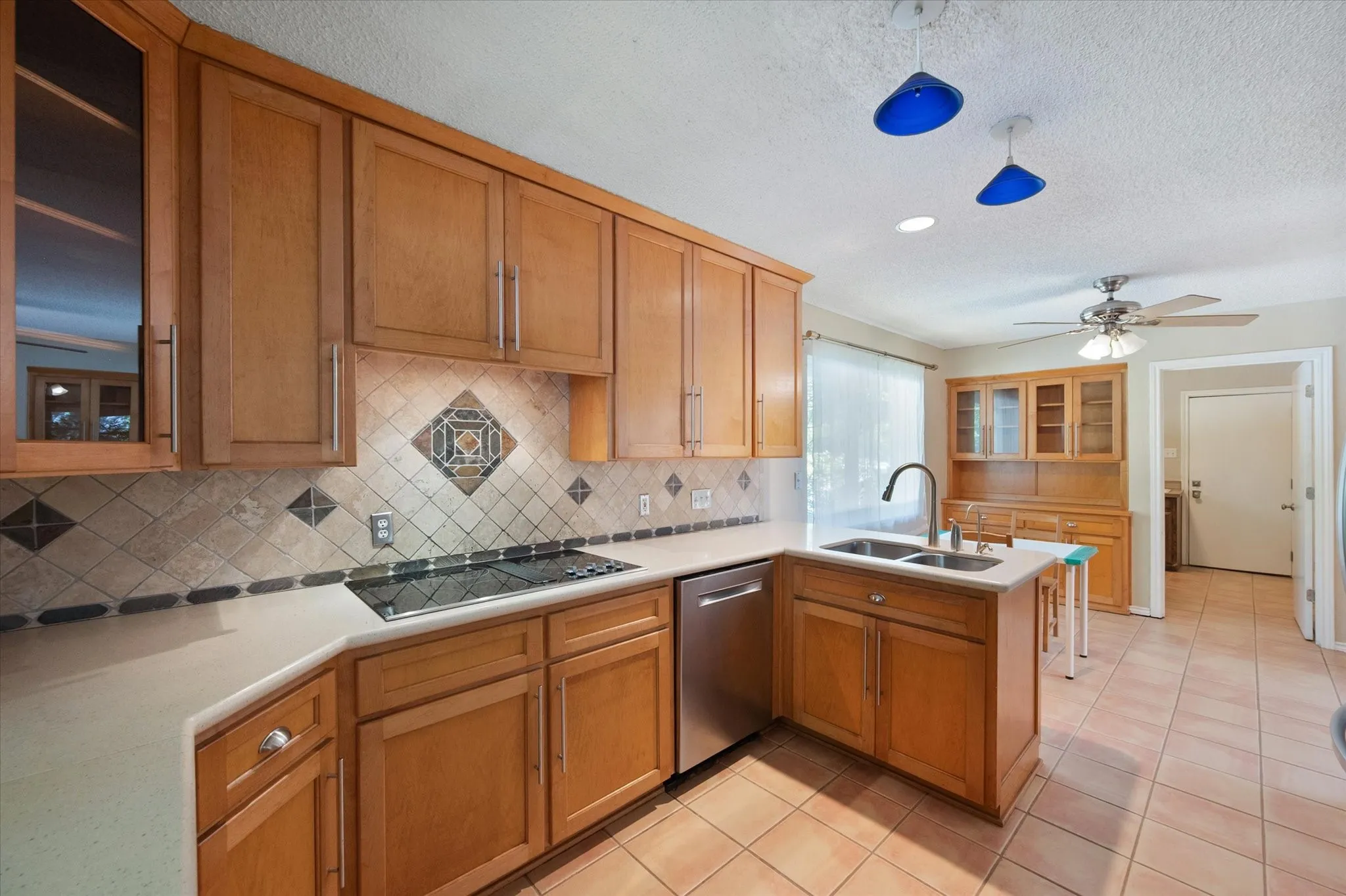 Kitchen featuring wood cabinetry, stone-tile backsplash, solid-surface countertops, stainless steel dishwasher, and ceramic tile flooring