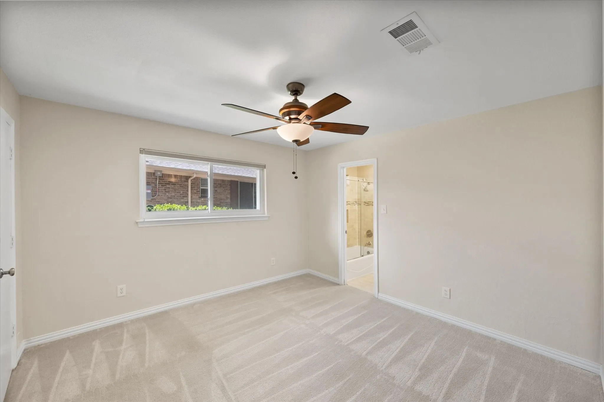 Neutral wall-to-wall carpeting, ceiling fan with integrated lighting, horizontal sliding window, and solid-core interior door