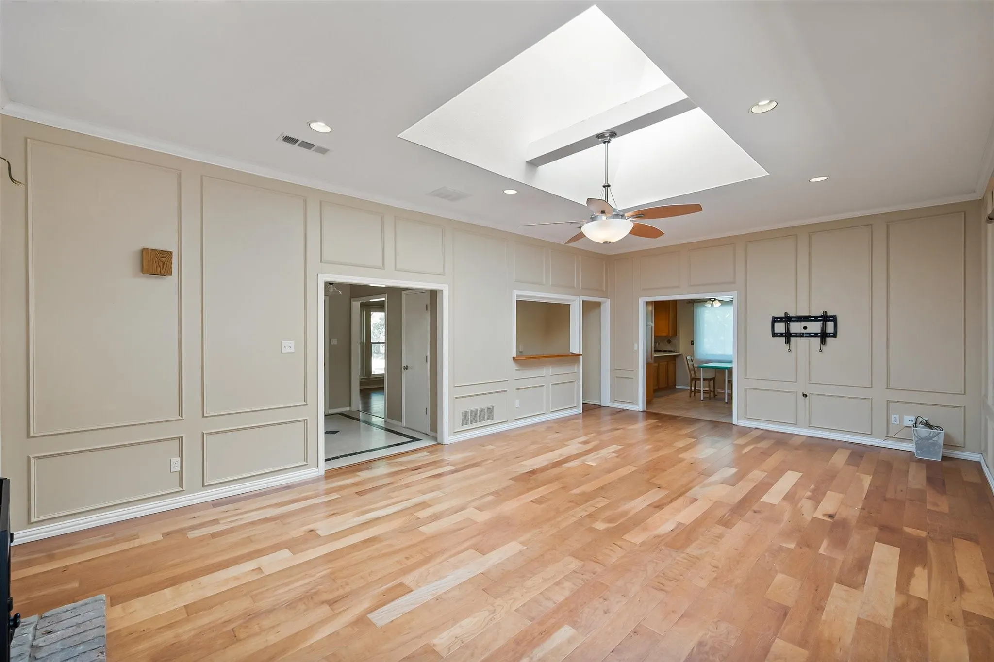 Living area featuring wood-finish flooring, extensive wall paneling, a ceiling skylight, recessed lighting, and a ceiling fan