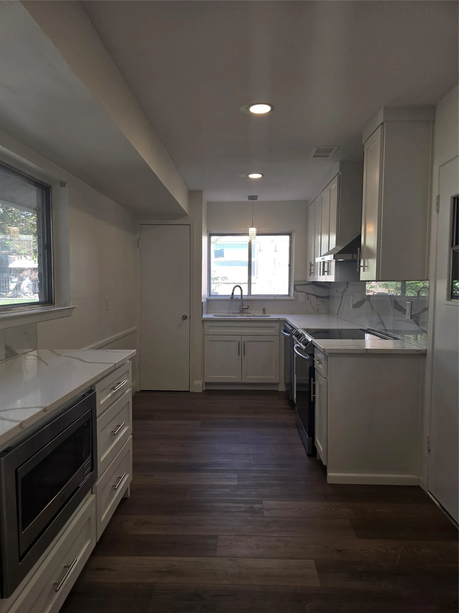 Kitchen featuring white shaker-style cabinetry, stone-patterned countertops, a full-height backsplash, stainless steel appliances, and dark wood-finish flooring