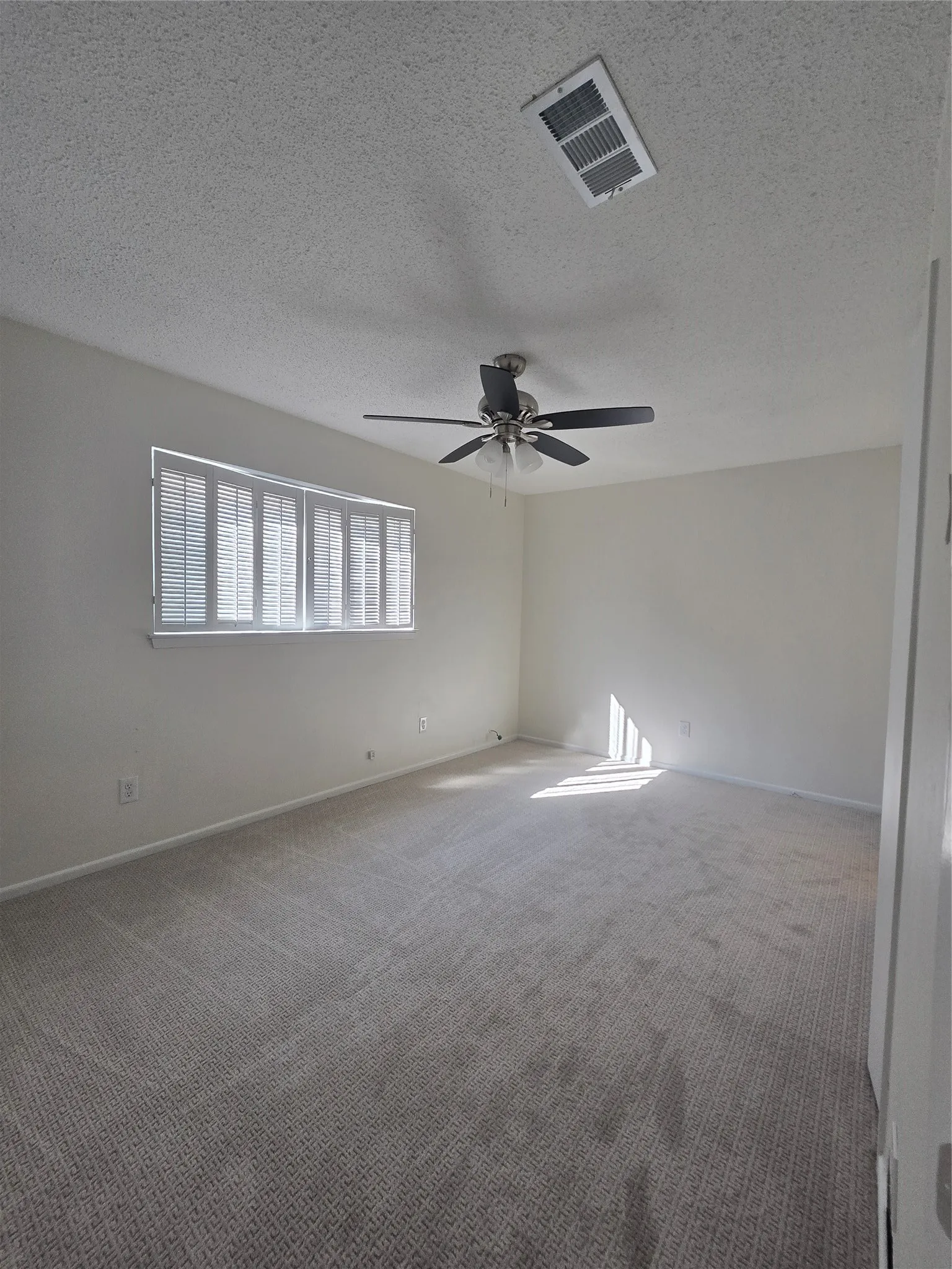Interior room featuring wall-to-wall carpeting, neutral wall coloring, a multi-blade ceiling fan with integrated lighting, and plantation-style window shutters