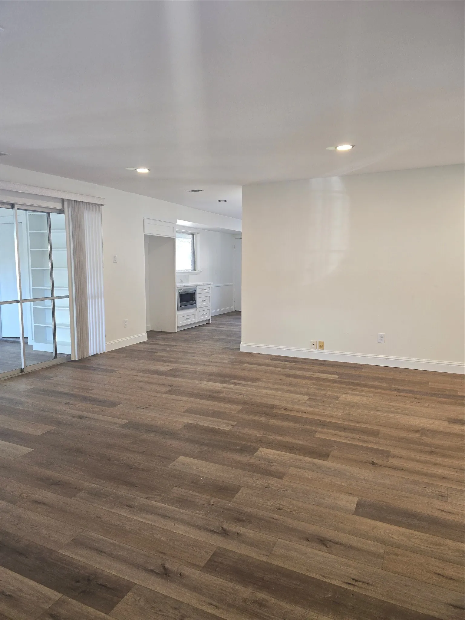 Open floor plan featuring wood-finish flooring, recessed lighting, sliding glass doors, and built-in shelving