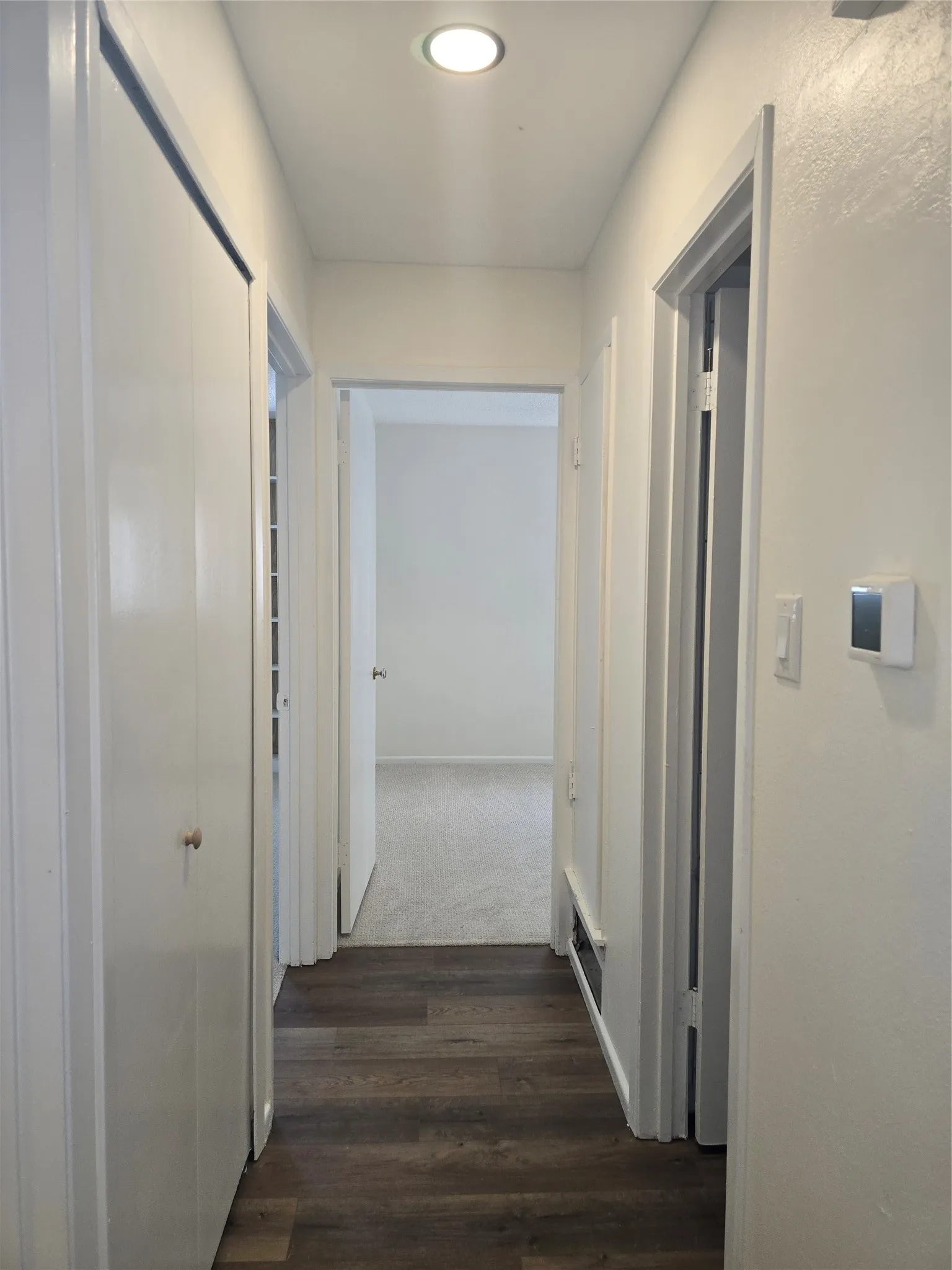 Hallway featuring wood-finish flooring, recessed ceiling lighting, a built-in closet with double-panel doors, and a wall-mounted thermostat