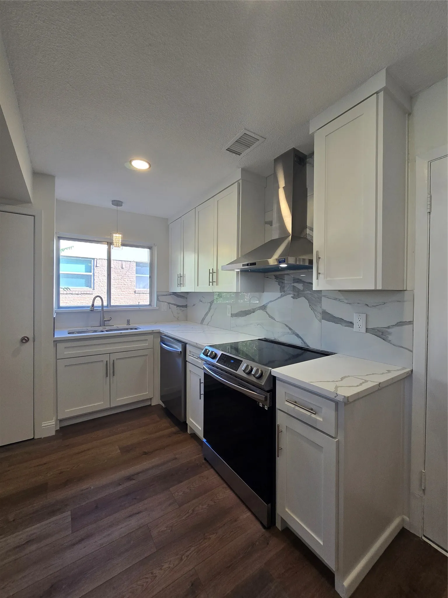 Kitchen featuring white shaker-style cabinetry, stone-patterned countertops, a full-height stone-patterned backsplash, stainless steel range with overhead chimney hood, and wood-finish flooring