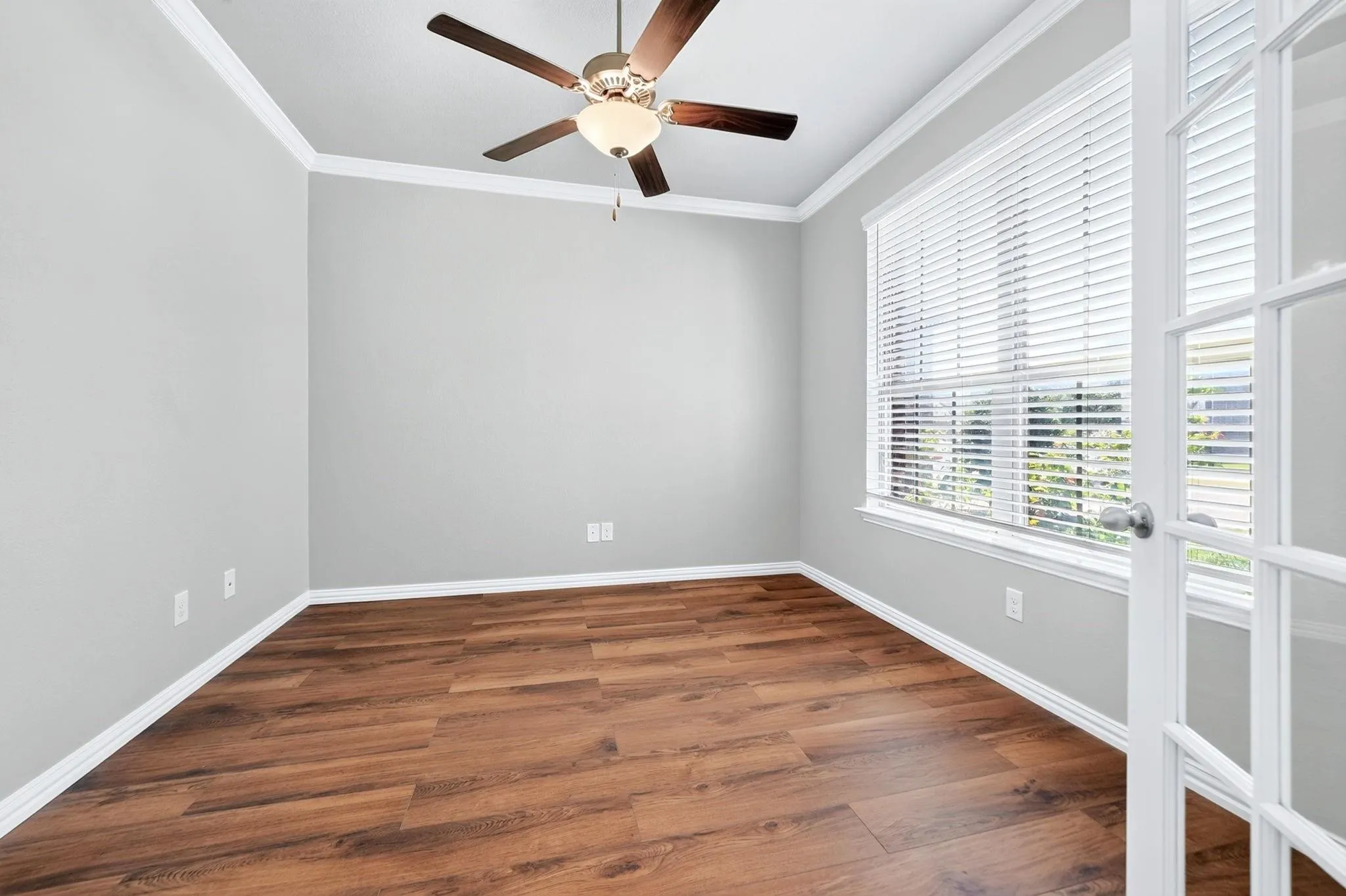 Room featuring wood-finish flooring, crown molding, a multi-pane glass door, and a ceiling fan with integrated lighting