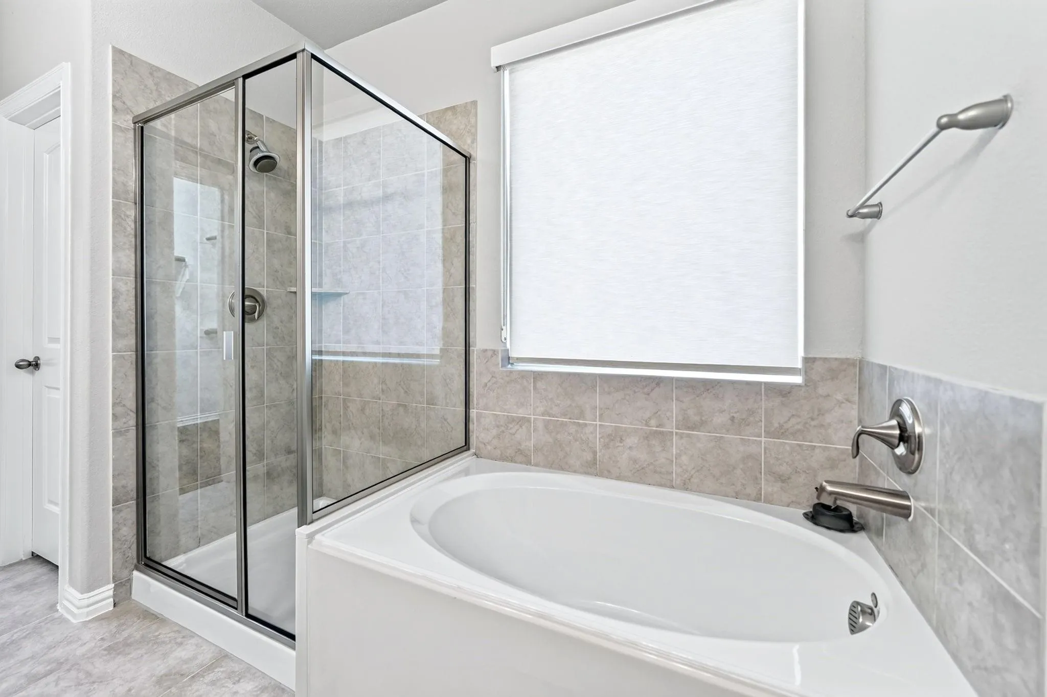 Enclosed glass shower with chrome fixtures and an oval soaking tub surrounded by neutral-toned wall tile