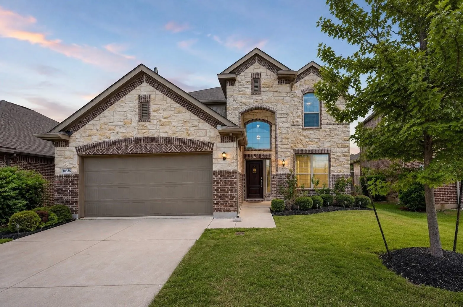 Multi-story exterior featuring a stone and brick facade, arched window detailing, covered entryway, and an attached two-car garage