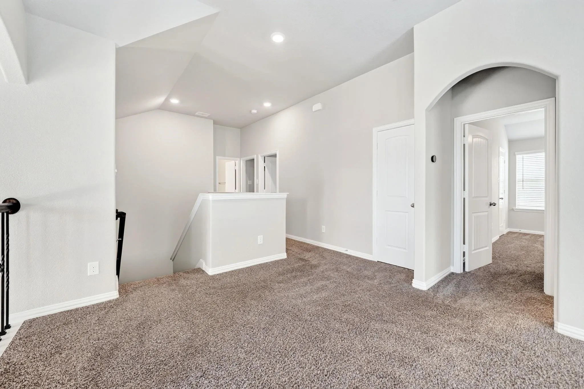Vaulted ceiling with recessed lighting, neutral wall palette, carpeted flooring, and an arched entry