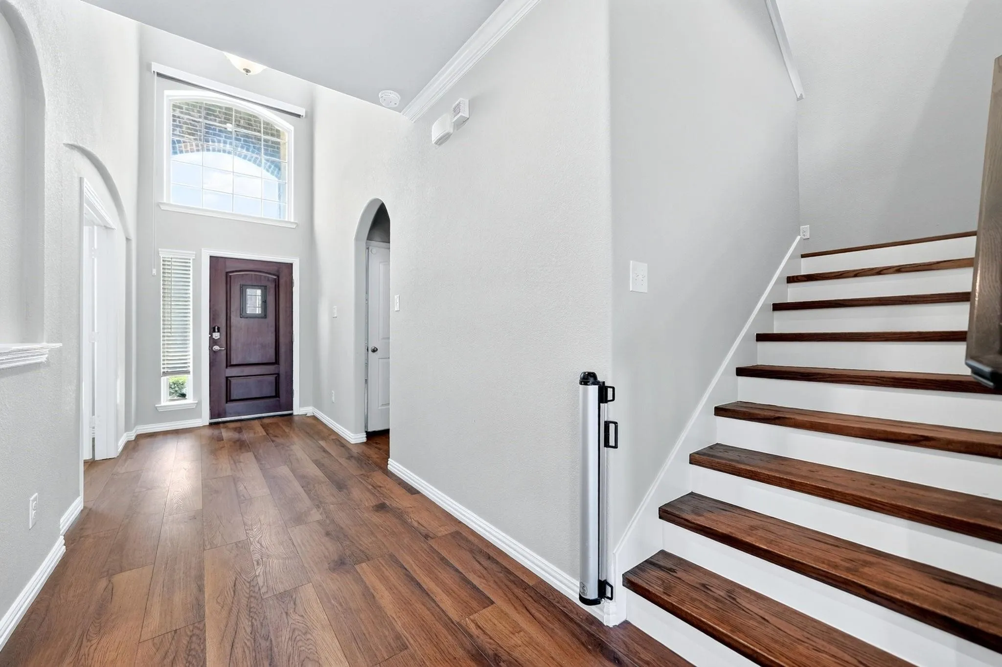 Foyer featuring high ceilings, wood-finish flooring, an arched doorway, a transom window, and a staircase with wood treads