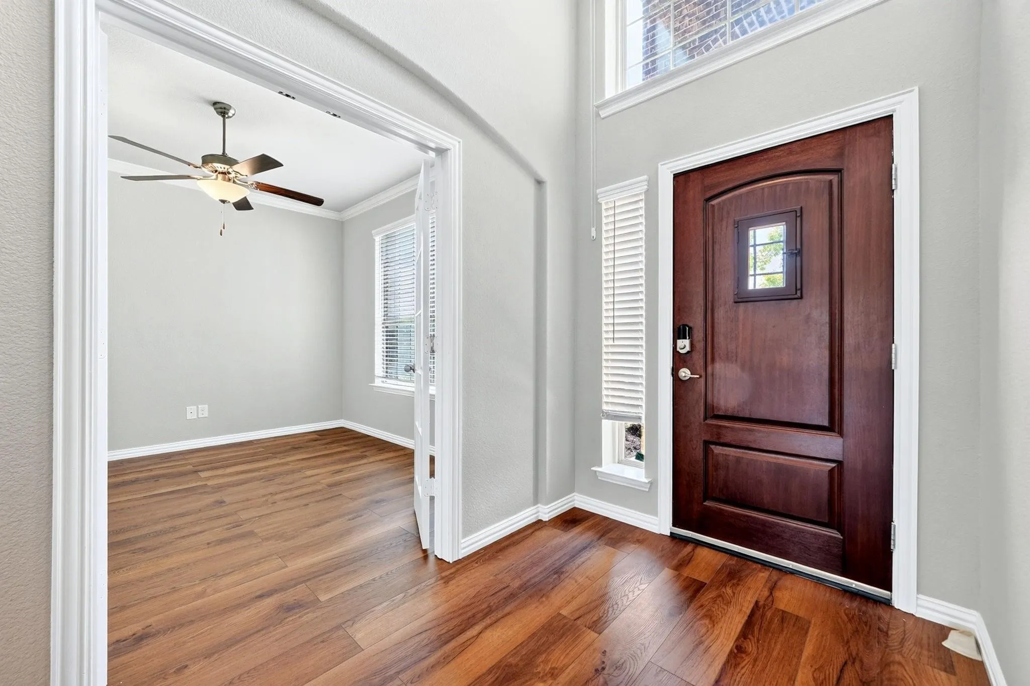 Entryway with high ceilings, wood-finish flooring, solid wood door with inset window, and double French doors opening to an auxiliary room with a ceiling fan