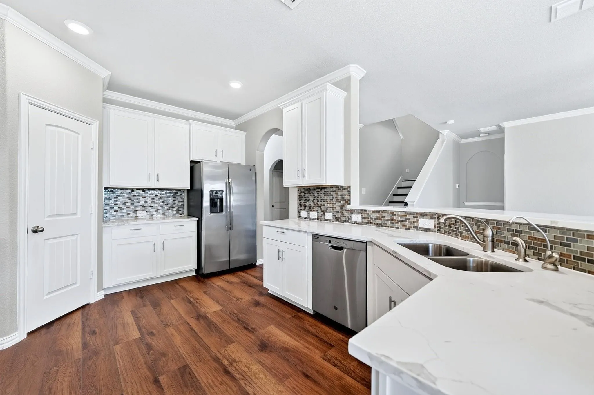 Kitchen featuring white cabinetry, solid-surface countertops with marbled pattern, stainless steel appliances, multi-toned mosaic tile backsplash, and wood-finish flooring