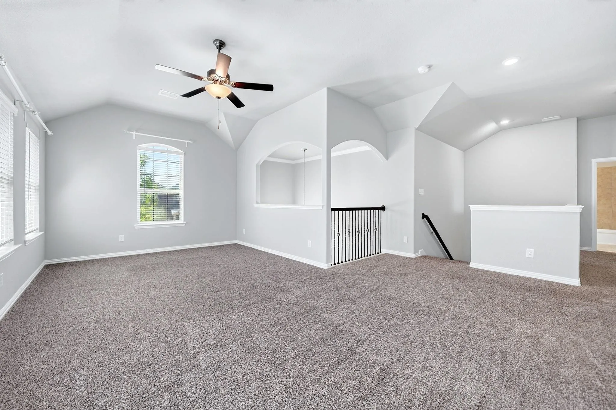 Vaulted ceilings with recessed lighting, wall-to-wall carpeting, archway architectural detailing, metal spindle railing, and a ceiling fan