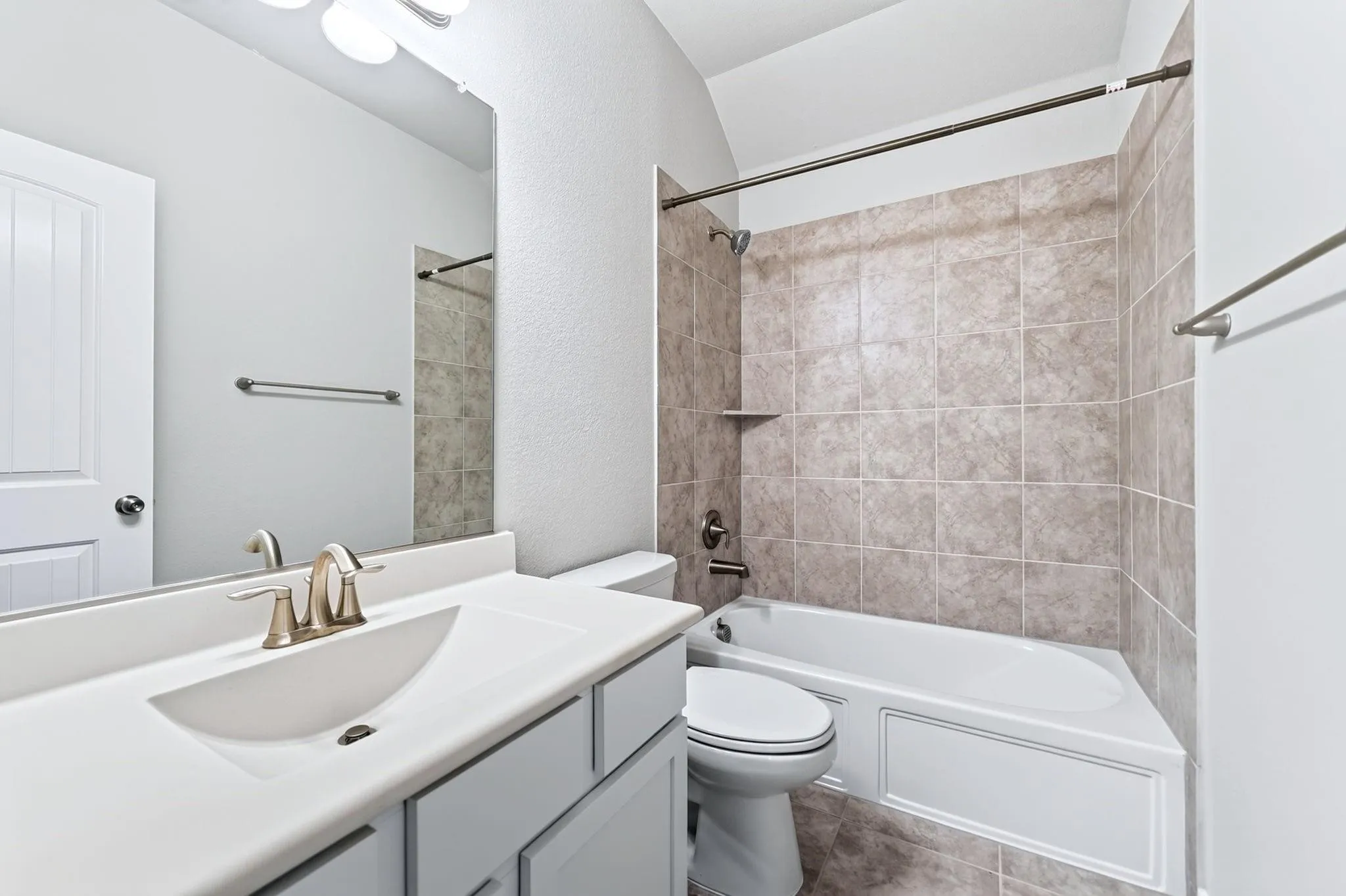 Bathroom featuring a vanity with an integrated sink, brushed-finish faucet, large mirror, and a tub-shower combination with ceramic tile surround