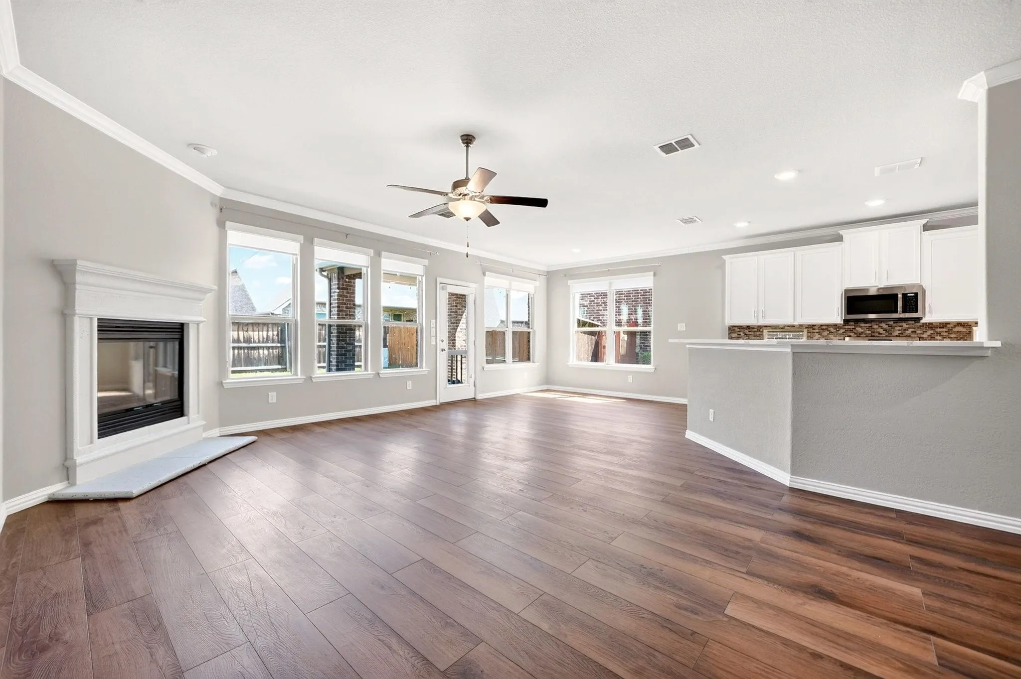 Open-concept living space featuring wood-finish flooring, a fireplace with a white mantel, ceiling fan, recessed lighting, and a kitchen equipped with white cabinetry and a breakfast bar