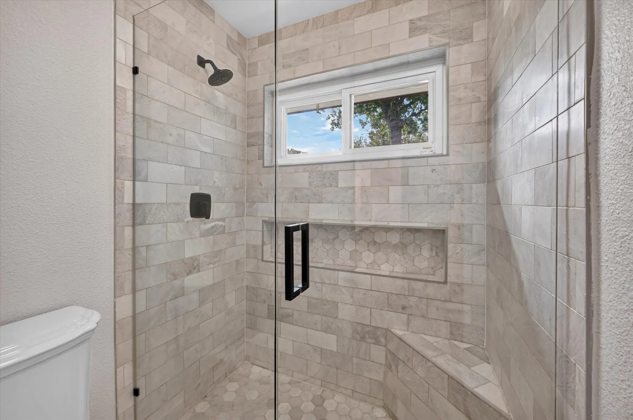 Downstairs ensuite surrounds, hexagonal tile flooring, a built-in bench, recessed shower niche, and matte black hardware