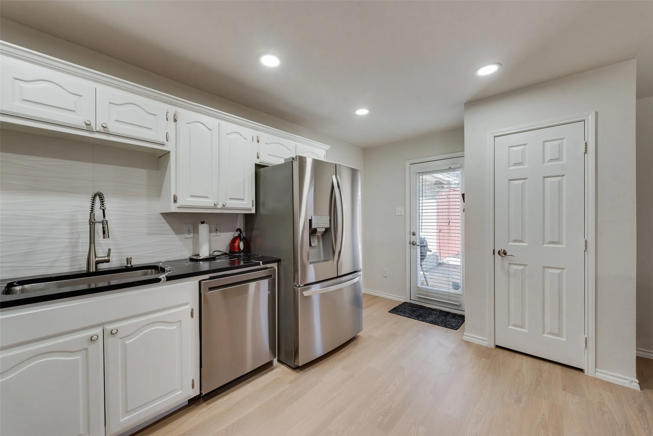 Kitchen featuring white cabinetry, dark countertops, stainless steel appliances, wood-finish flooring, and recessed lighting