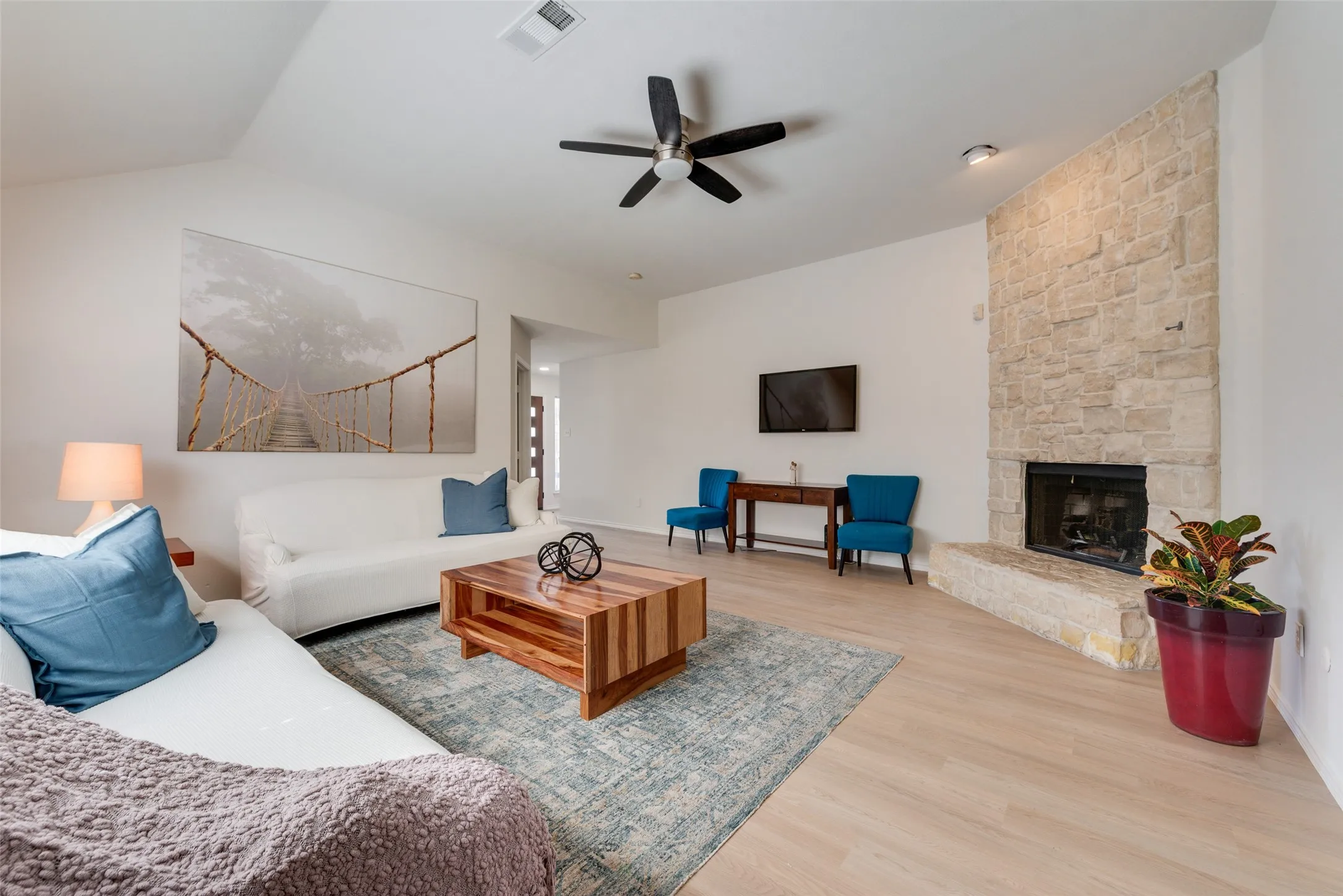 Living area featuring high ceilings, wood-finish flooring, and a full-height stone-veneer fireplace with a raised hearth