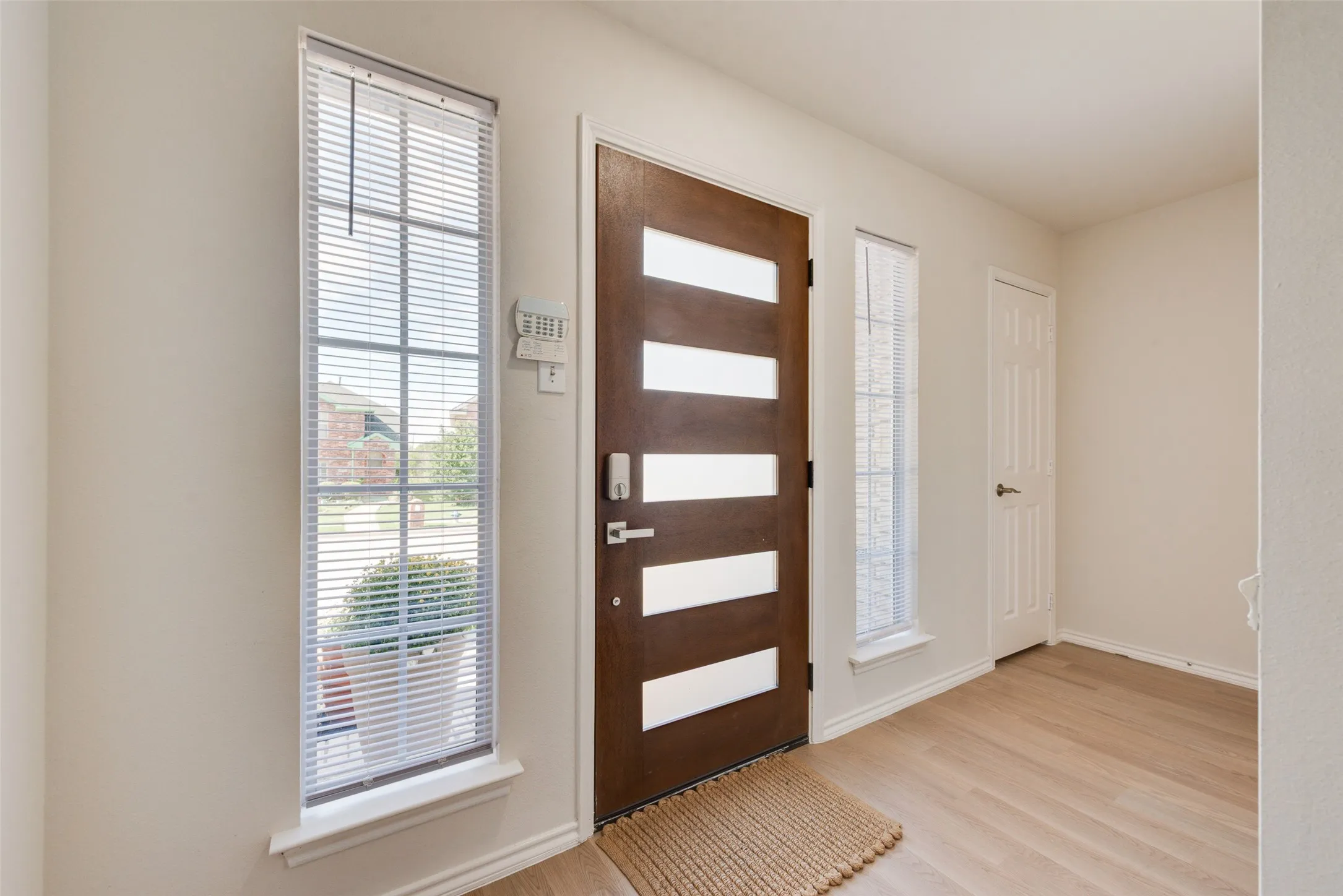 Entryway featuring a wood-finish door with horizontal glass panels, flanked by two tall windows, wood-finish flooring, and a six-panel door