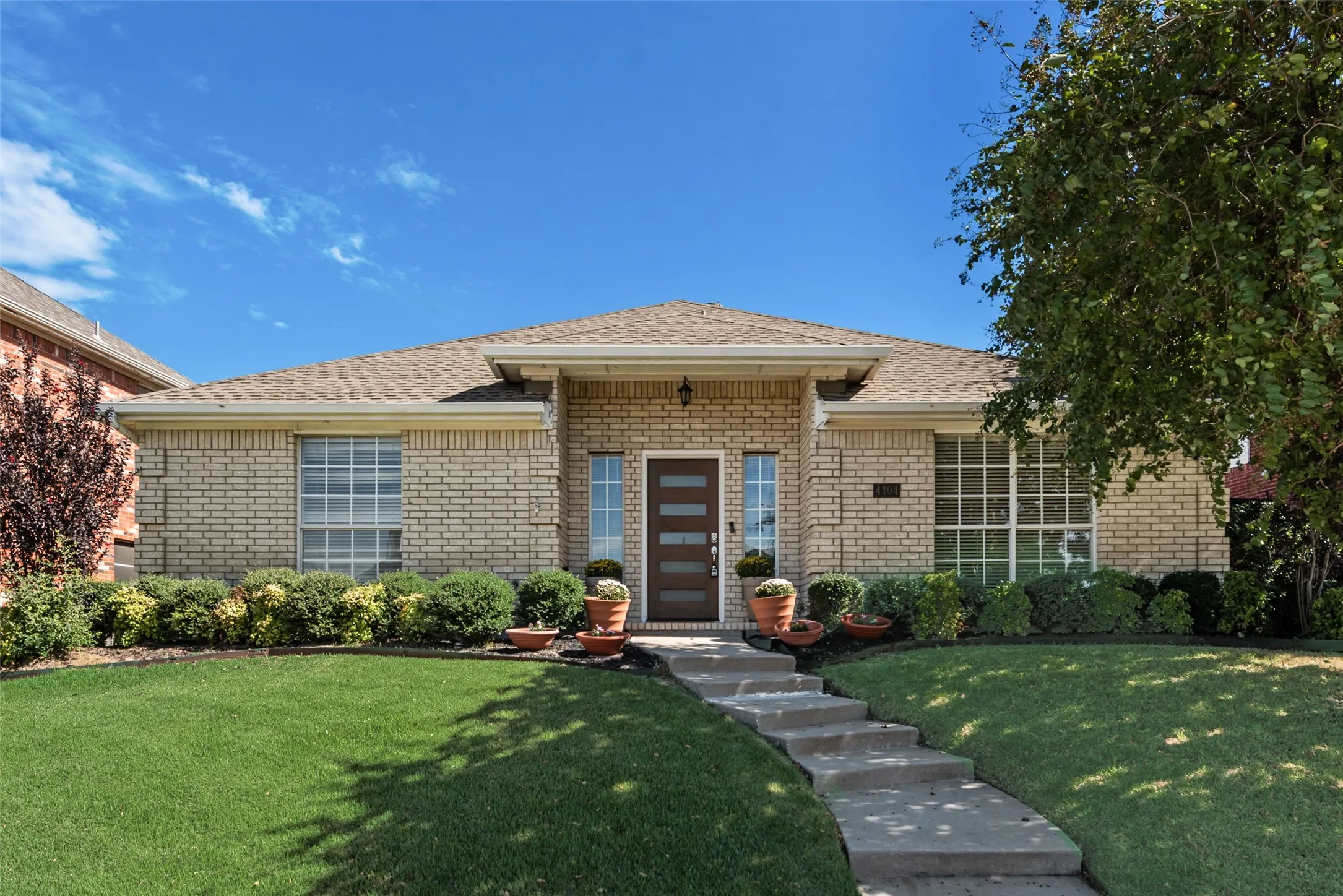 Single-story exterior featuring light brick masonry, a hipped roof, grid-pattern windows, and a modern front door with horizontal glass panels