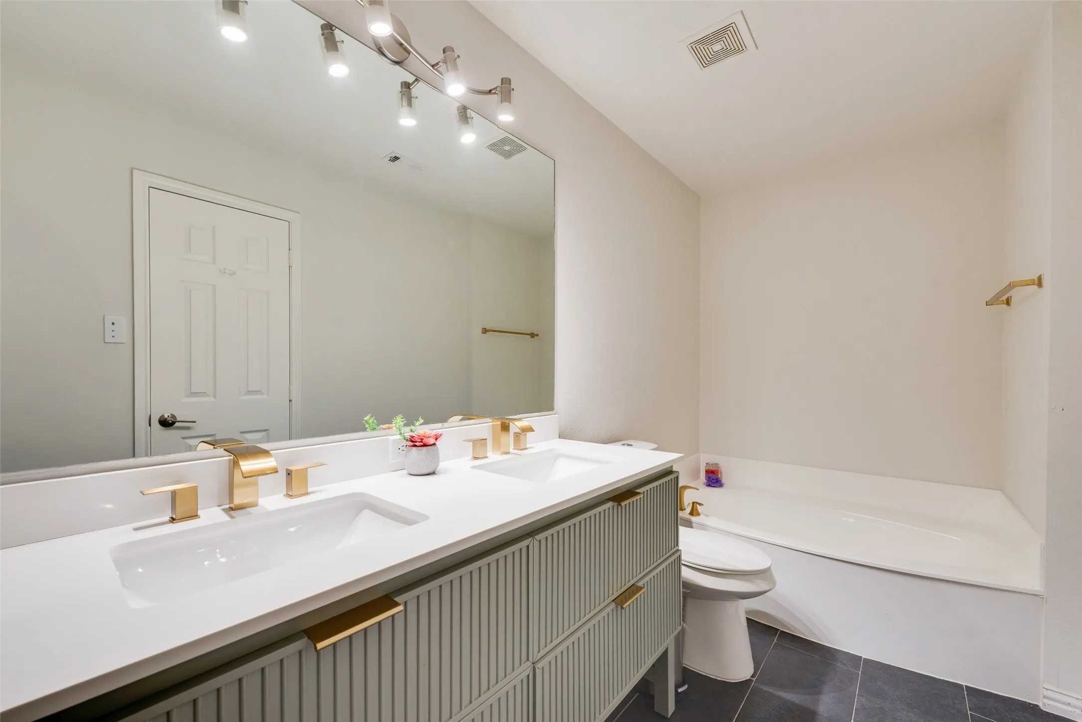 Dual-sink vanity with ribbed cabinetry, white countertops, brass-finish fixtures, and a large wall-mounted mirror