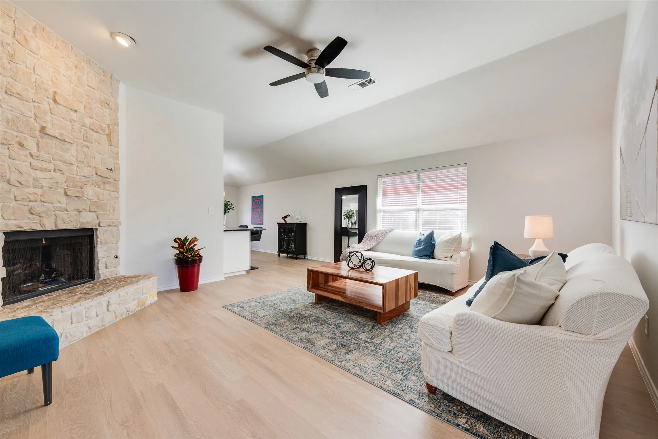 Stone-clad fireplace with a raised hearth, wood-finish flooring, vaulted ceiling, and ceiling fan