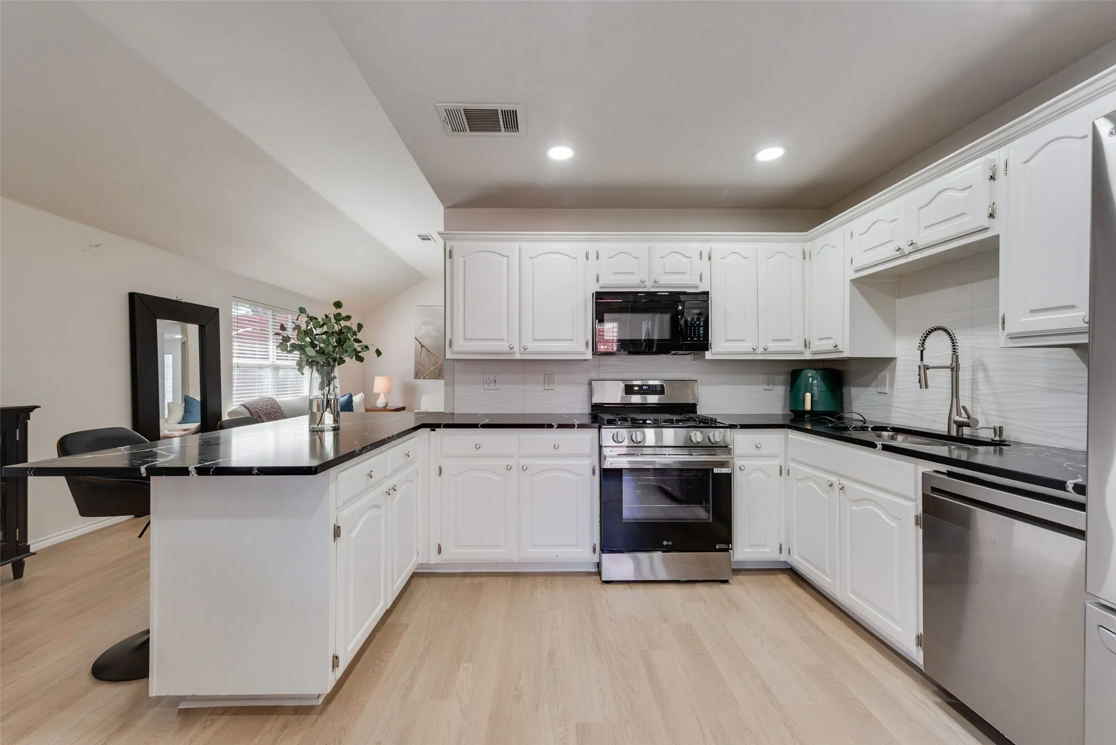 Kitchen featuring white cabinetry, dark stone-finish countertops, stainless steel appliances, and wood-finish flooring