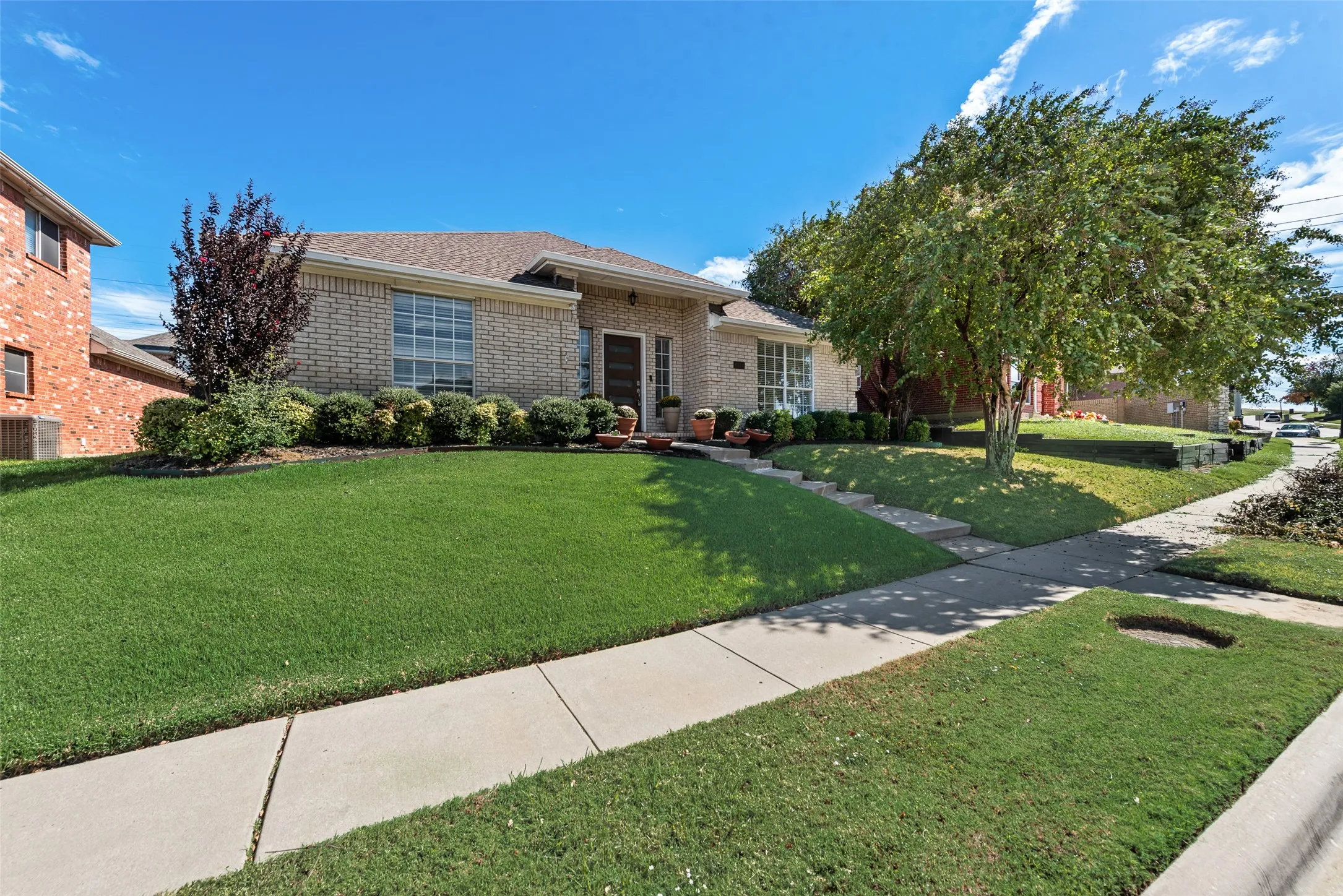 Single-story brick exterior featuring a hipped roofline, manicured lawn, and mature shade trees