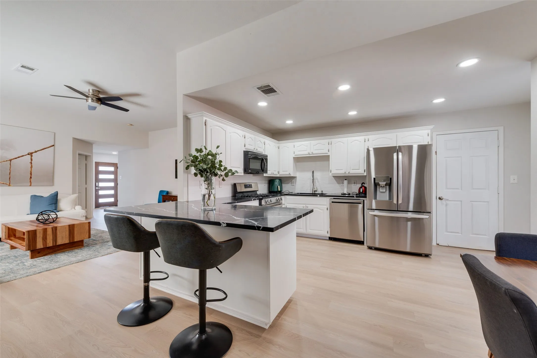 Kitchen featuring white cabinetry, dark stone-finish countertops, stainless steel appliances, a center island with a breakfast bar, and wood-finish flooring