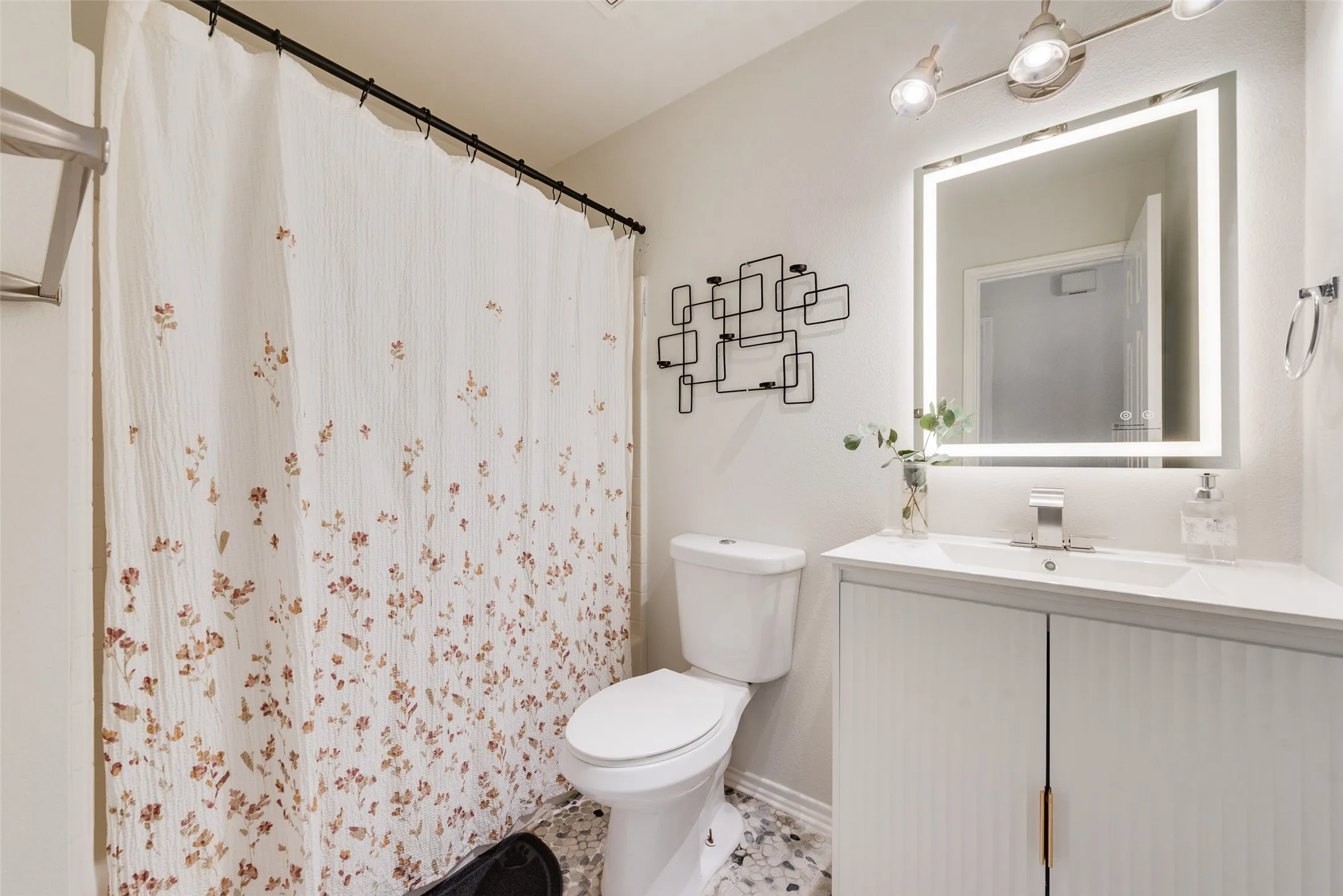 Bathroom featuring a vanity with vertical ribbed cabinet doors, a countertop with an integrated basin, a lighted mirror, and decorative wall-mounted metal shelving