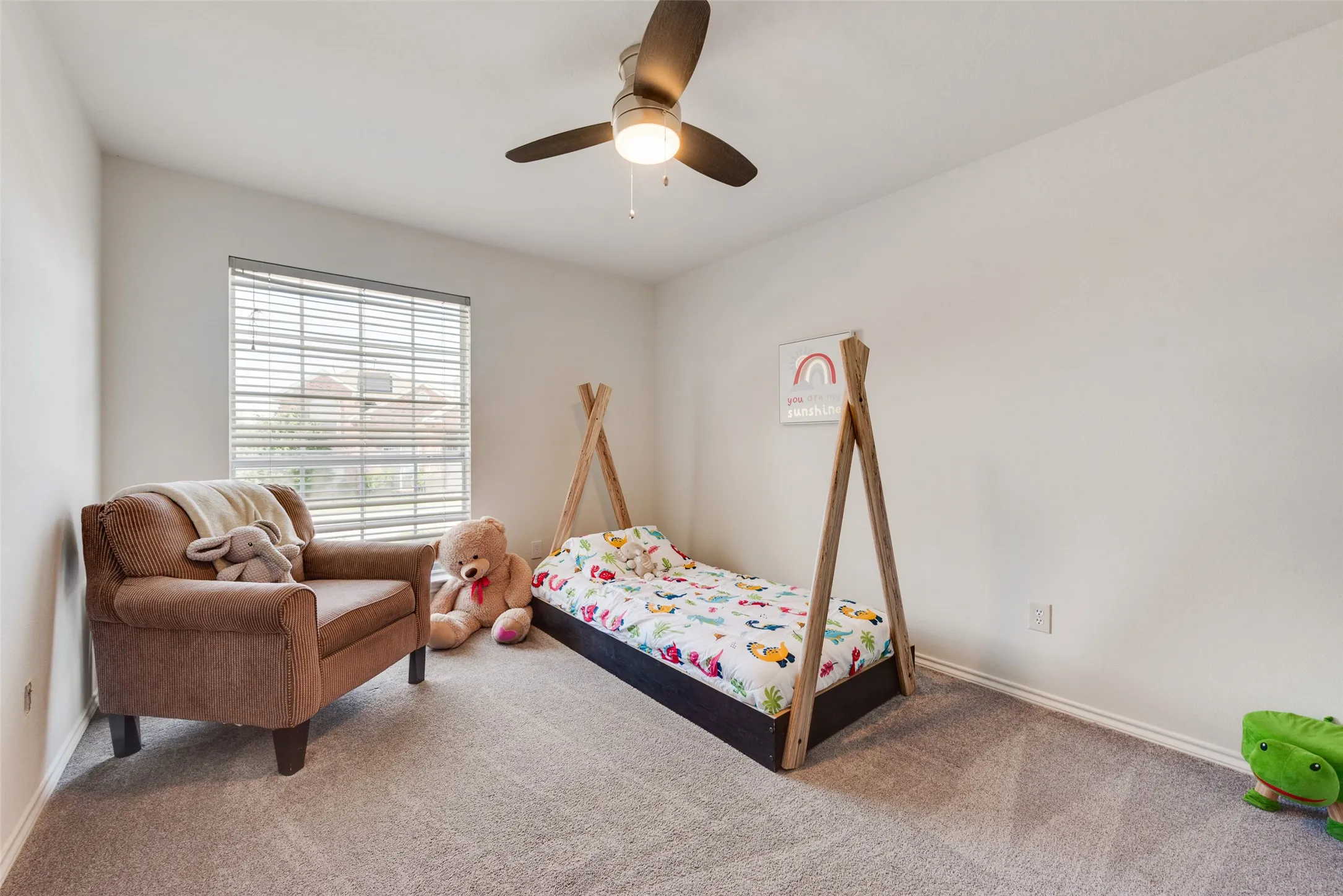Neutral-toned wall-to-wall carpeting, window with integrated horizontal blinds, and a three-blade ceiling fan with a center light fixture
