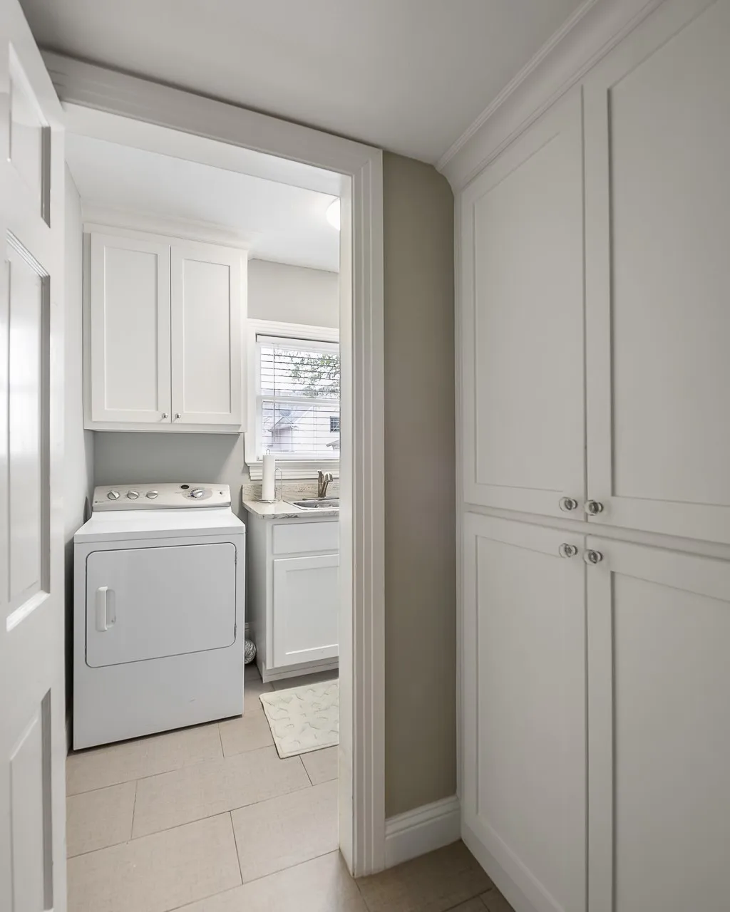 Utility space featuring white shaker-style cabinetry, floor-to-ceiling built-in storage, stone-surfaced countertop with undermount sink, and tile flooring