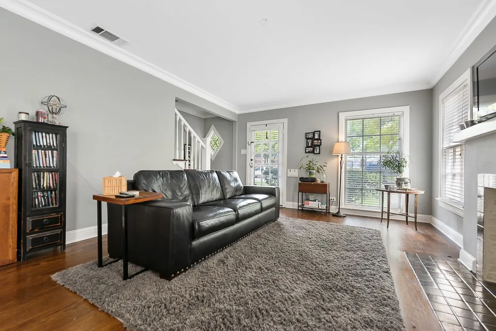 Living room featuring wood-finish flooring, crown molding, double-hung windows with integrated blinds, and a tiled fireplace surround