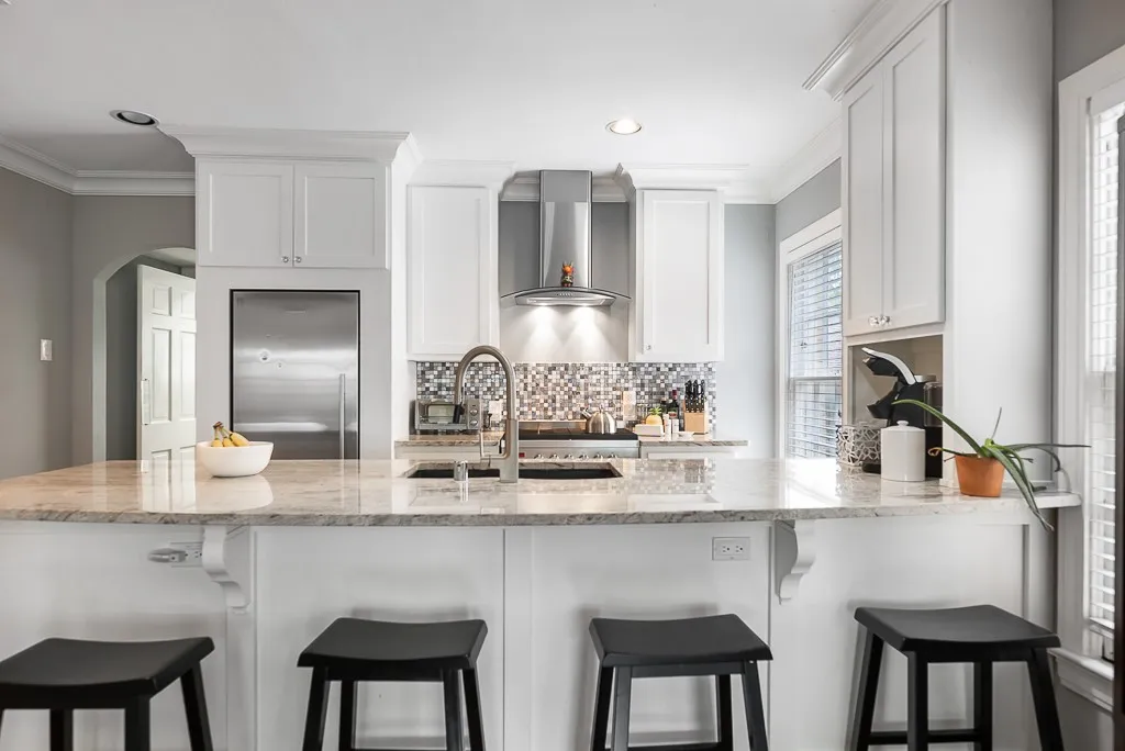 Kitchen featuring white cabinetry, stone countertops, a stainless steel range hood, a mosaic tile backsplash, and a central island with an integrated sink