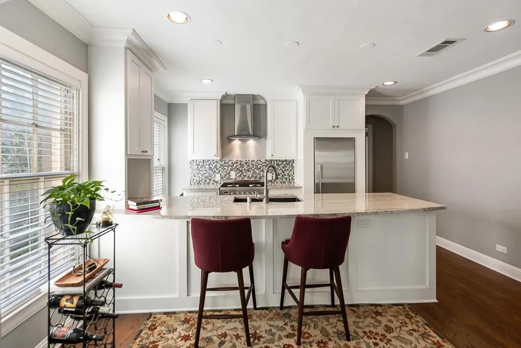 Kitchen featuring white shaker-style cabinetry, stone countertops, stainless steel appliances, a mosaic tile backsplash, and an island with a built-in sink