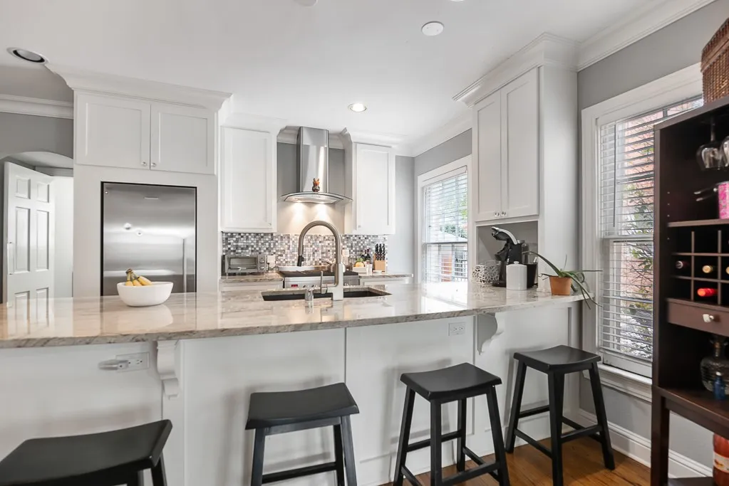 Kitchen featuring white shaker cabinetry, stone countertops, mosaic tile backsplash, stainless steel range hood, and wood-finish flooring