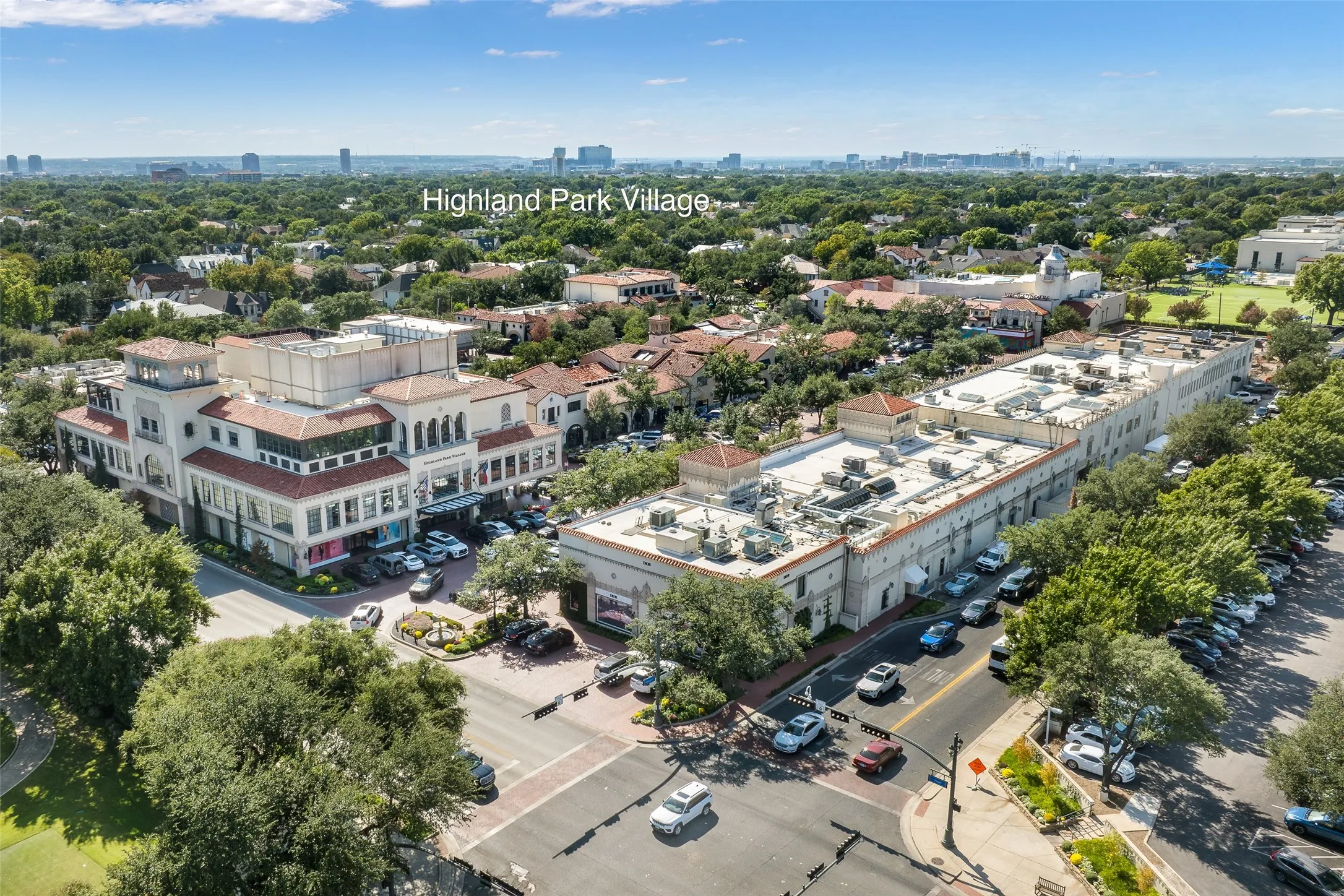 Aerial perspective of Highland Park Village featuring multi-level retail and office structures, Mediterranean-inspired architectural details, tile roofing, and paved surface parking