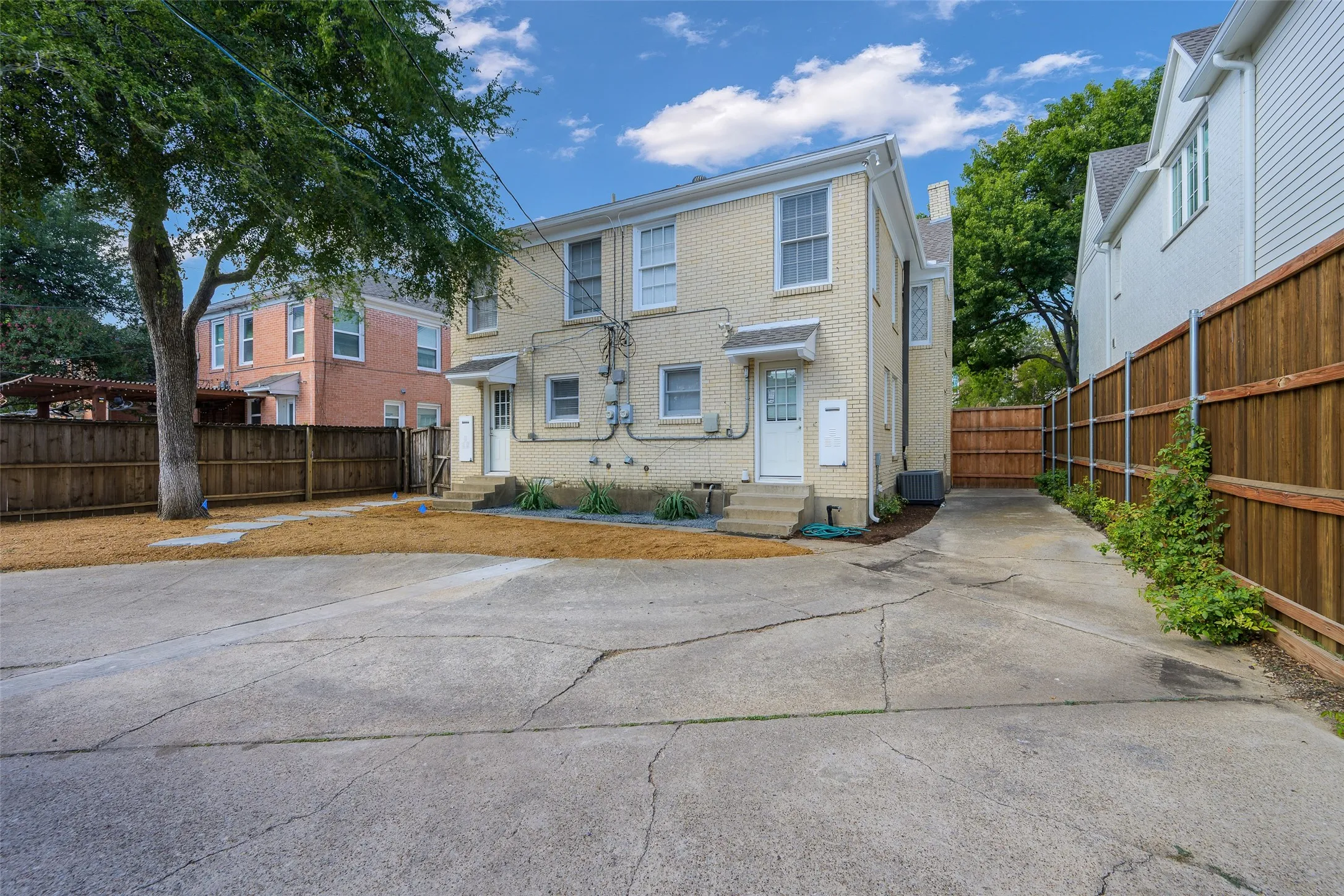 Exterior featuring light-colored brick siding, concrete parking area, and wood privacy fencing