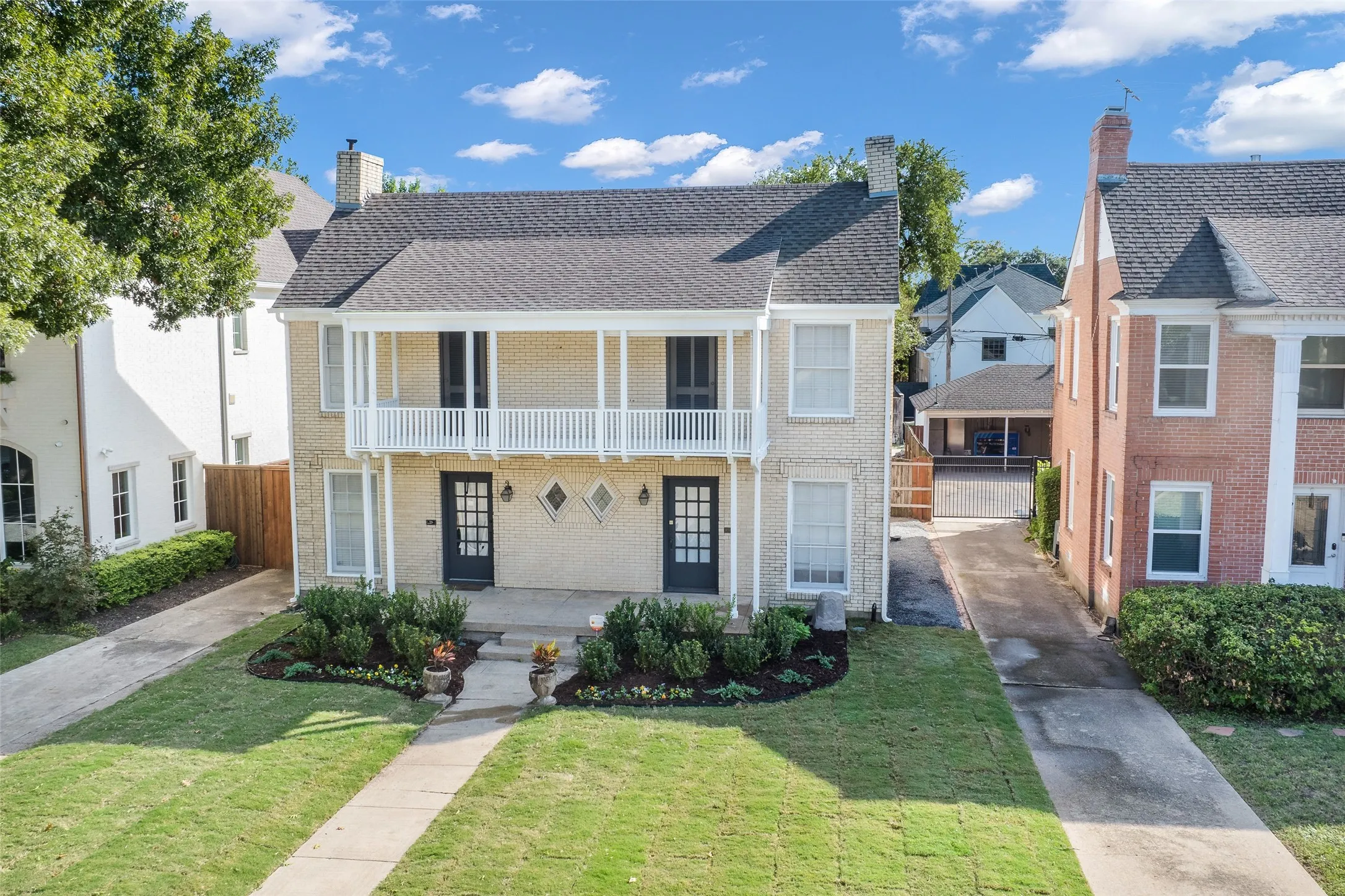 Traditional brick exterior featuring a covered upper-level balcony, dual-entry French doors, diamond-shaped accent windows, and a paved private driveway