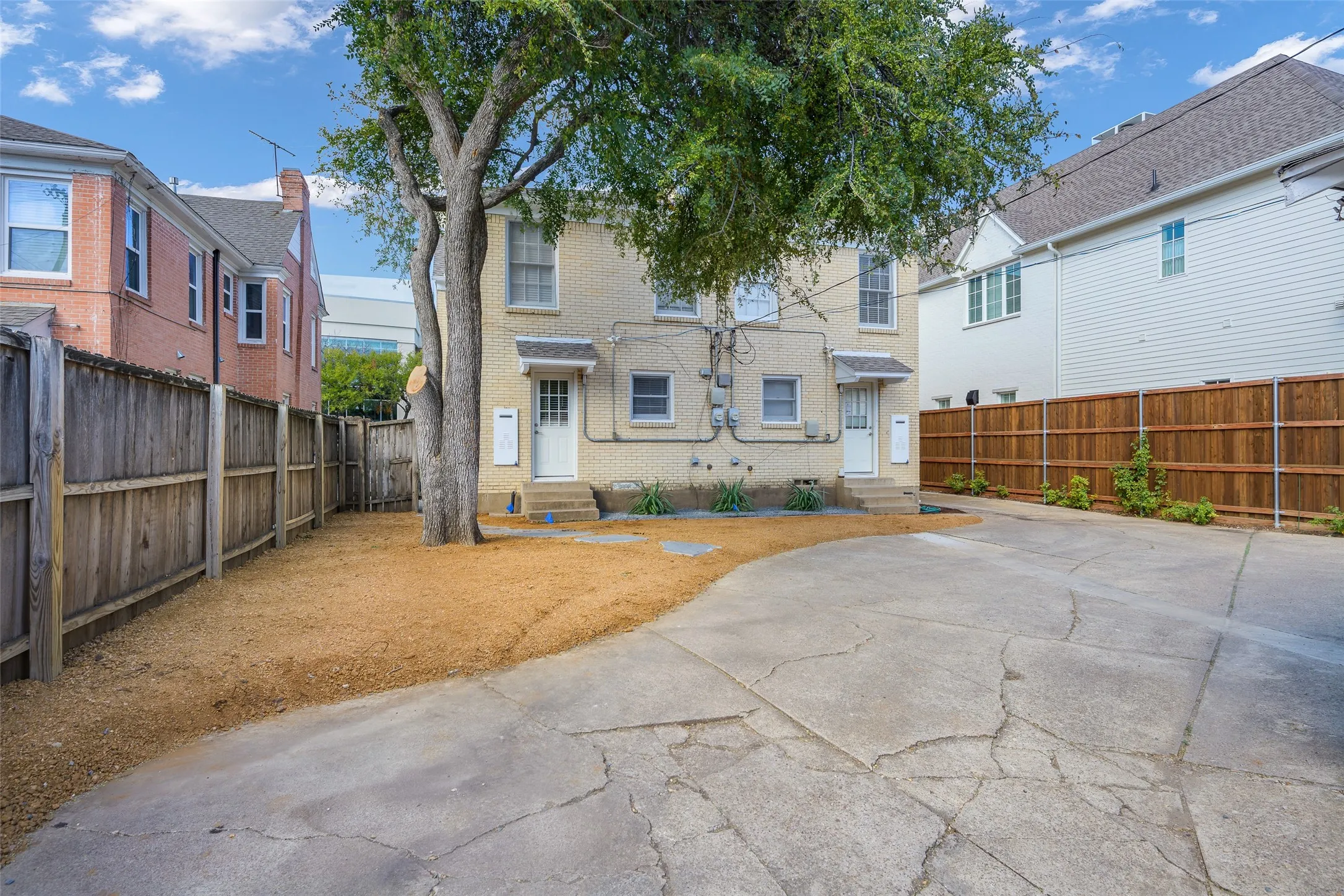 Two-story light brick exterior with a concrete parking area and wood-style privacy fencing
