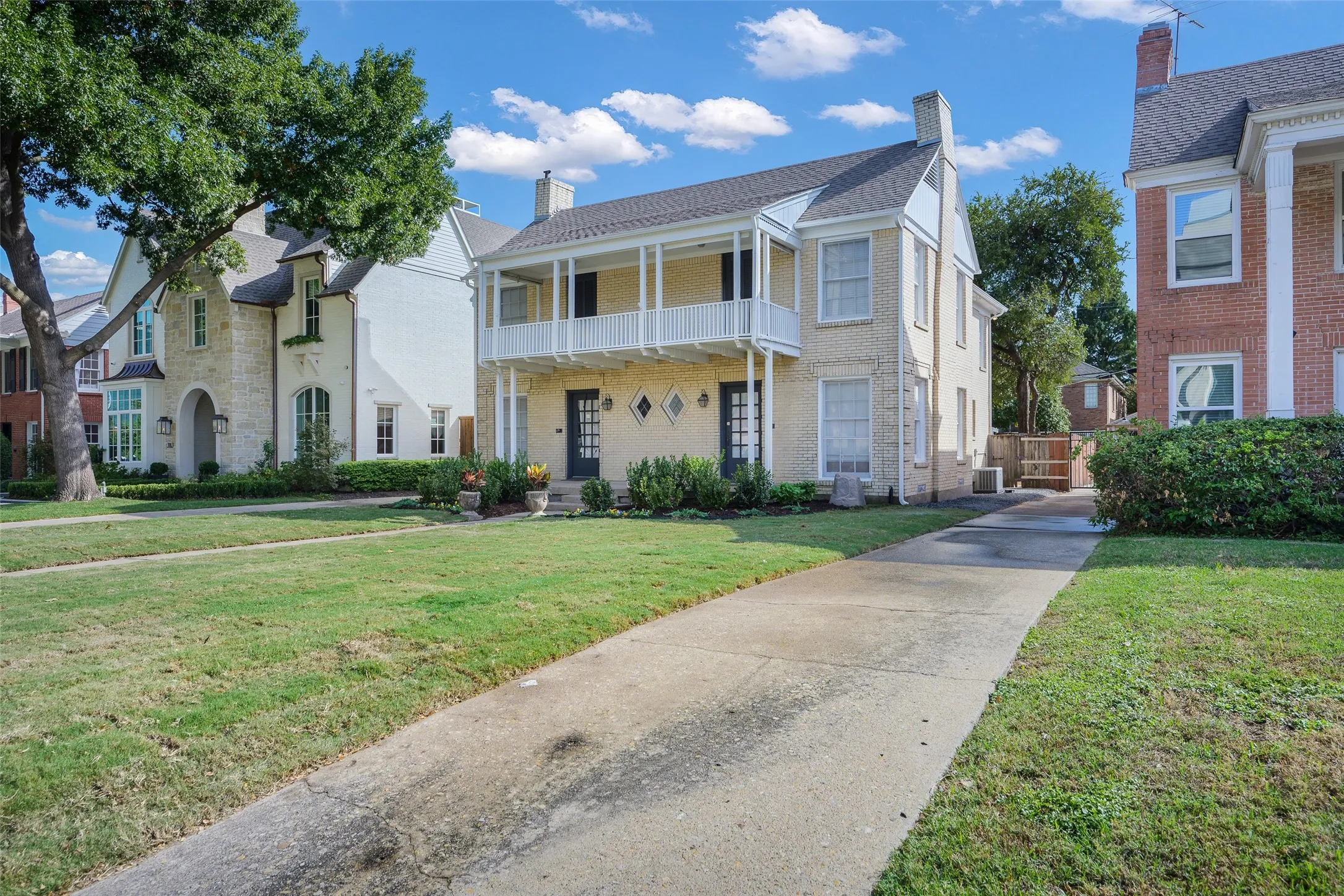 Brick exterior featuring a double-story covered balcony with decorative railings, symmetrical diamond-shaped windows, and a concrete driveway