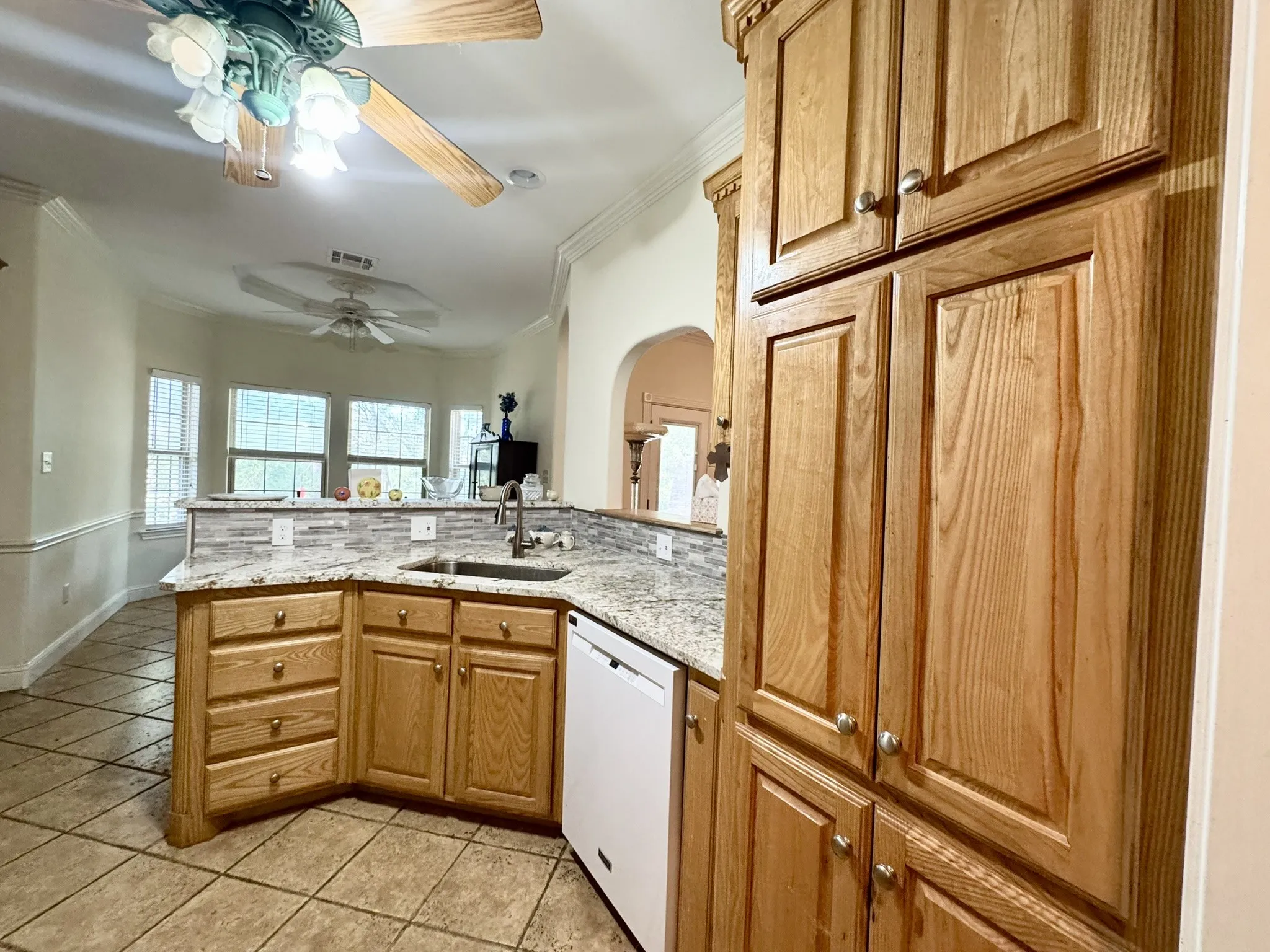 Kitchen featuring wood cabinetry, stone countertops, a mosaic tile backsplash, a stainless steel undermount sink with a pull-down faucet, and tiled flooring