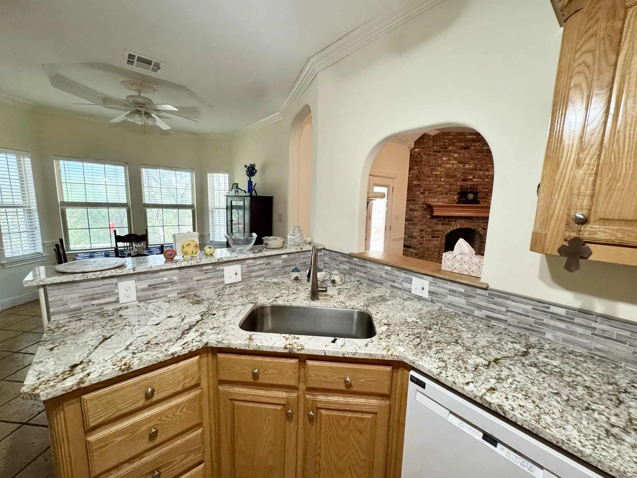 Kitchen featuring stone-finish countertops, mosaic tile backsplash, wood-finish cabinetry, stainless steel sink, and arched wall detailing
