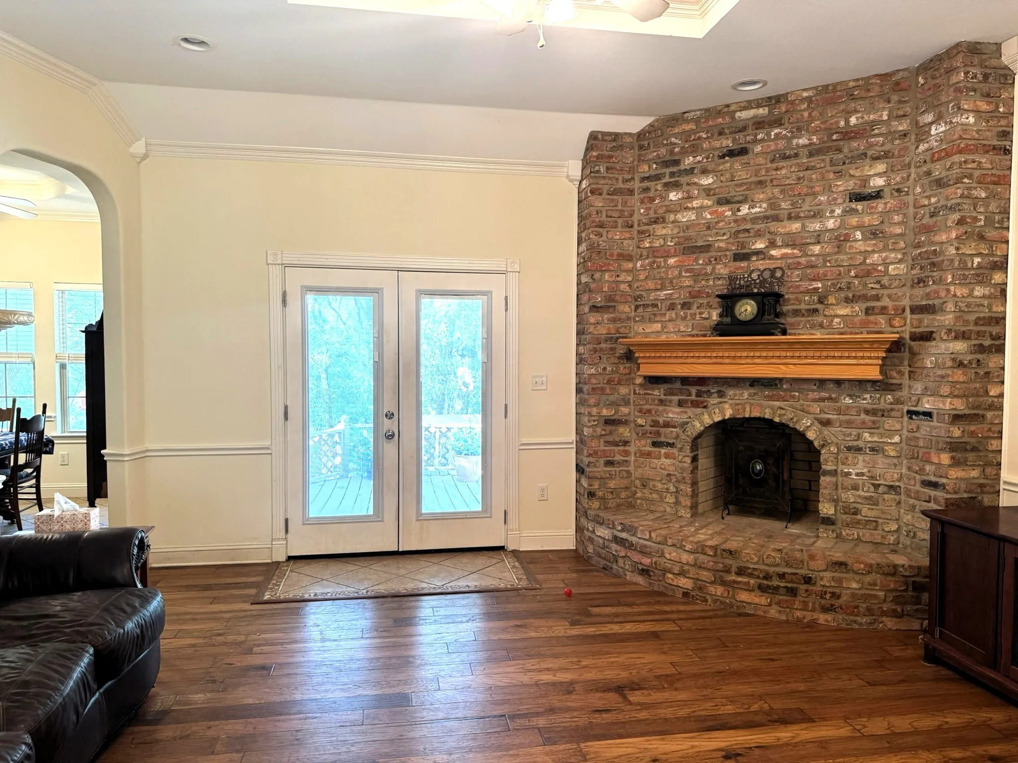 Floor-to-ceiling brick fireplace with an arched firebox and decorative wood mantel, wood-finish flooring, double glass-paneled doors, tray ceiling with recessed lighting, and crown molding